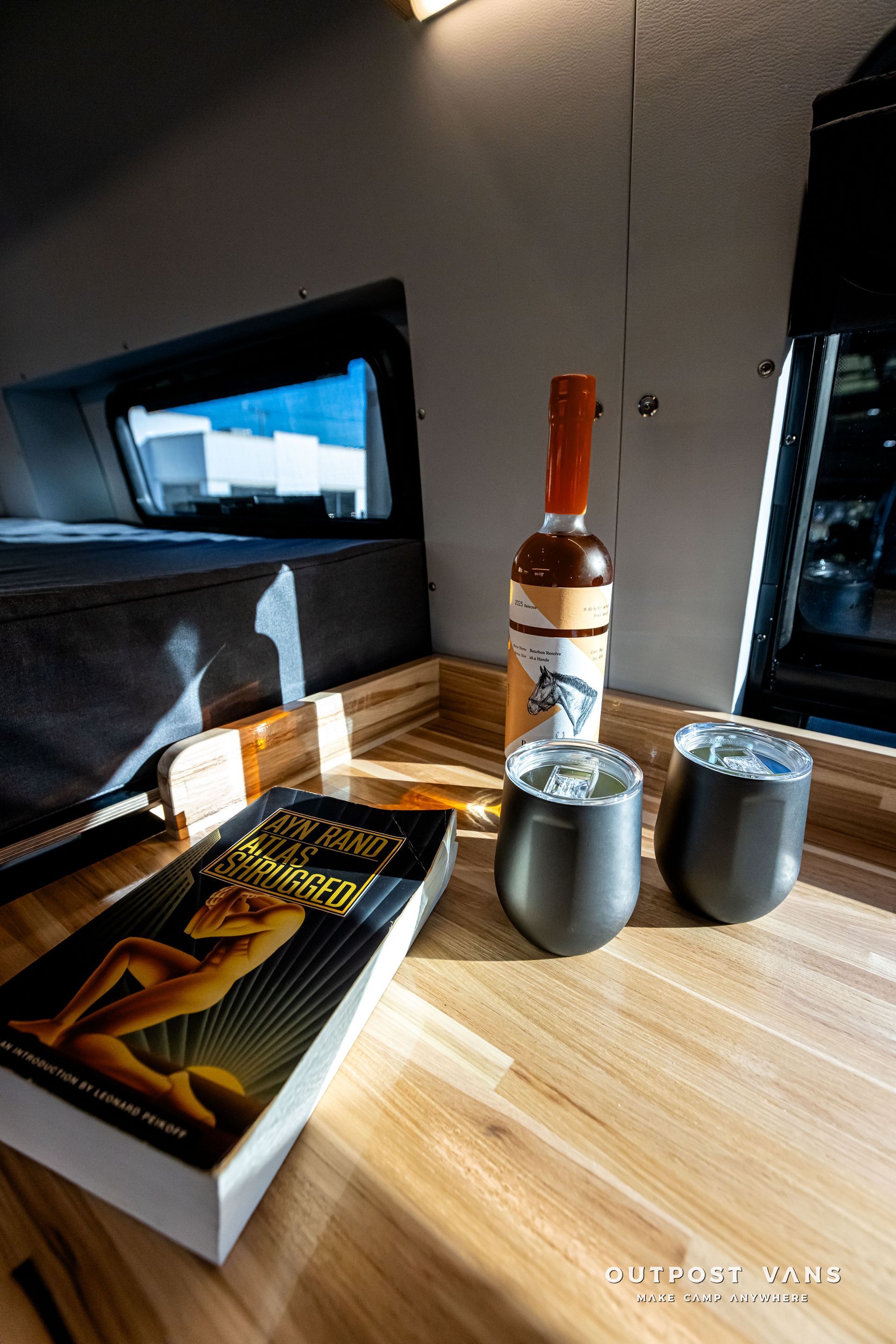 A bottle of wine is sitting on a wooden table next to two cups and a book.