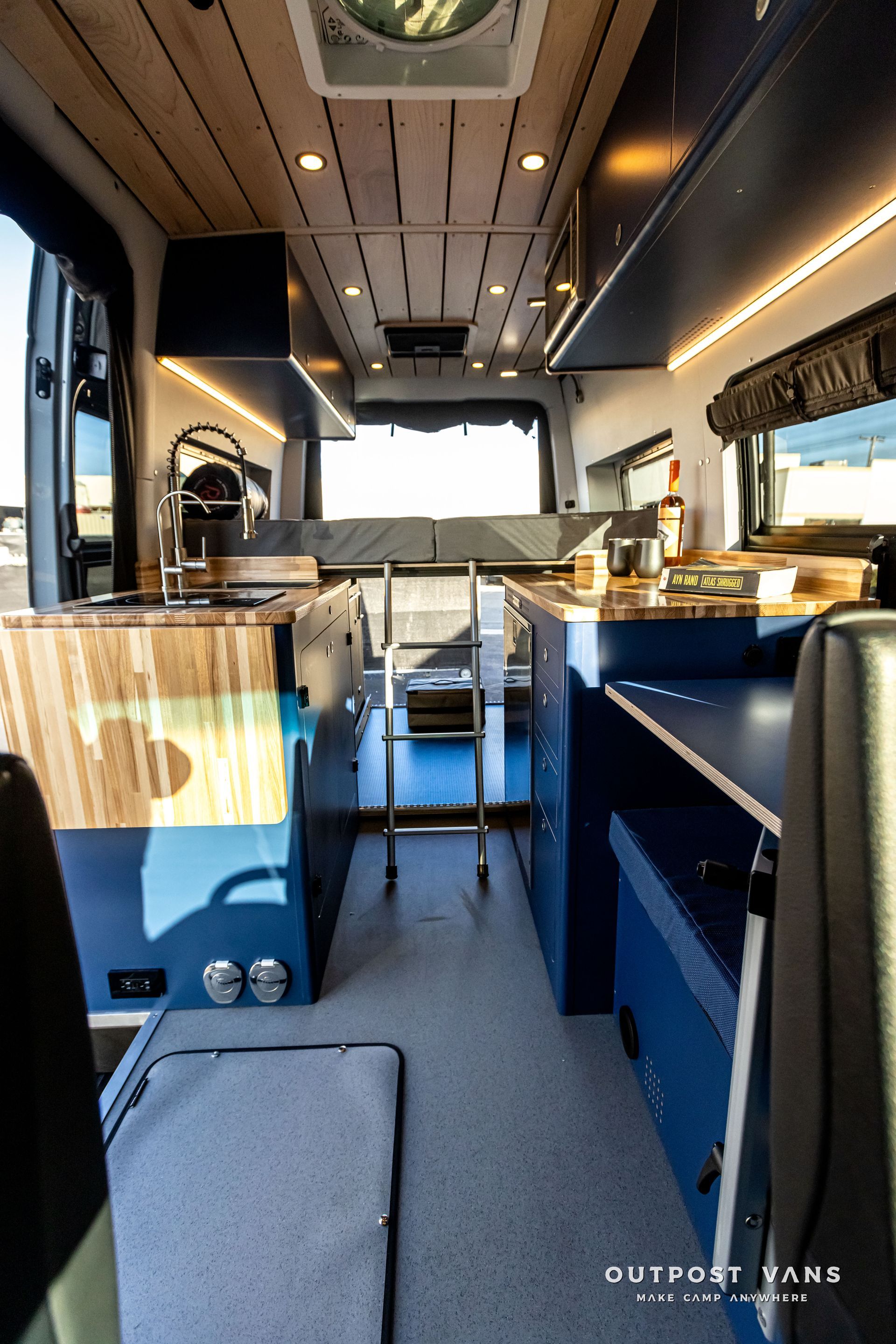 The inside of a van with a ladder and a fan on the ceiling.