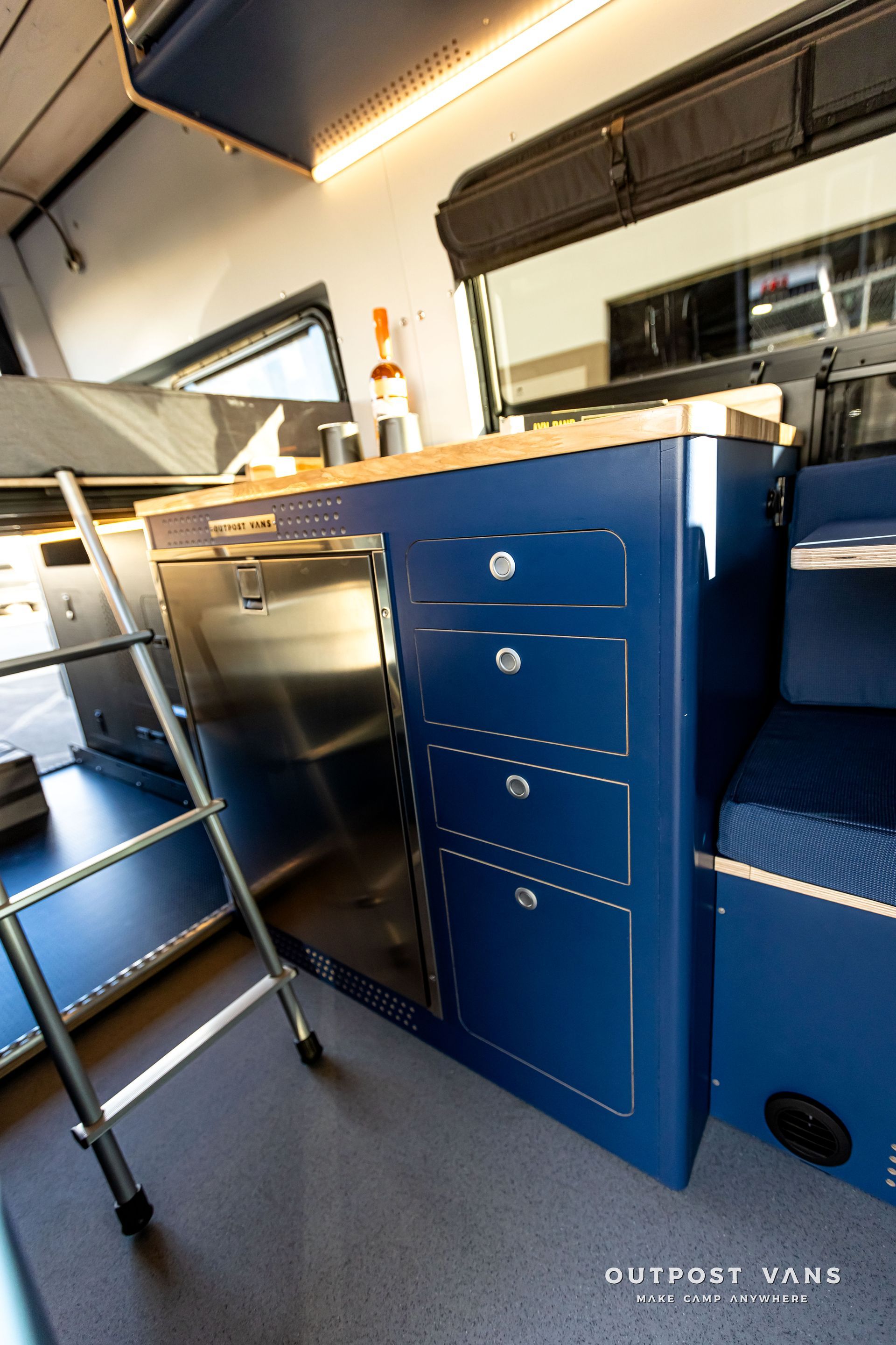 A kitchen in a van with blue cabinets and a ladder.