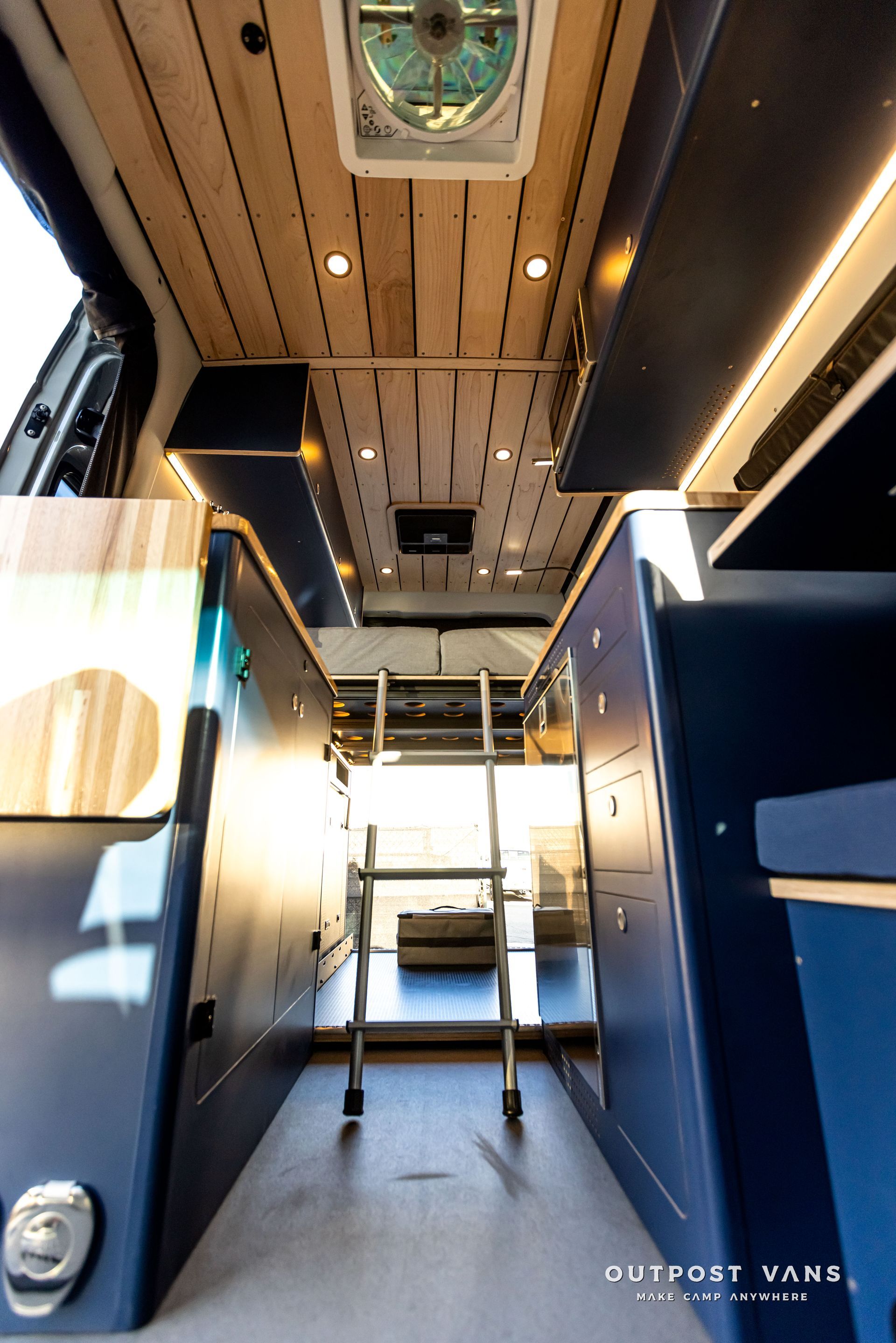 The inside of a van with a ladder and a fan on the ceiling.