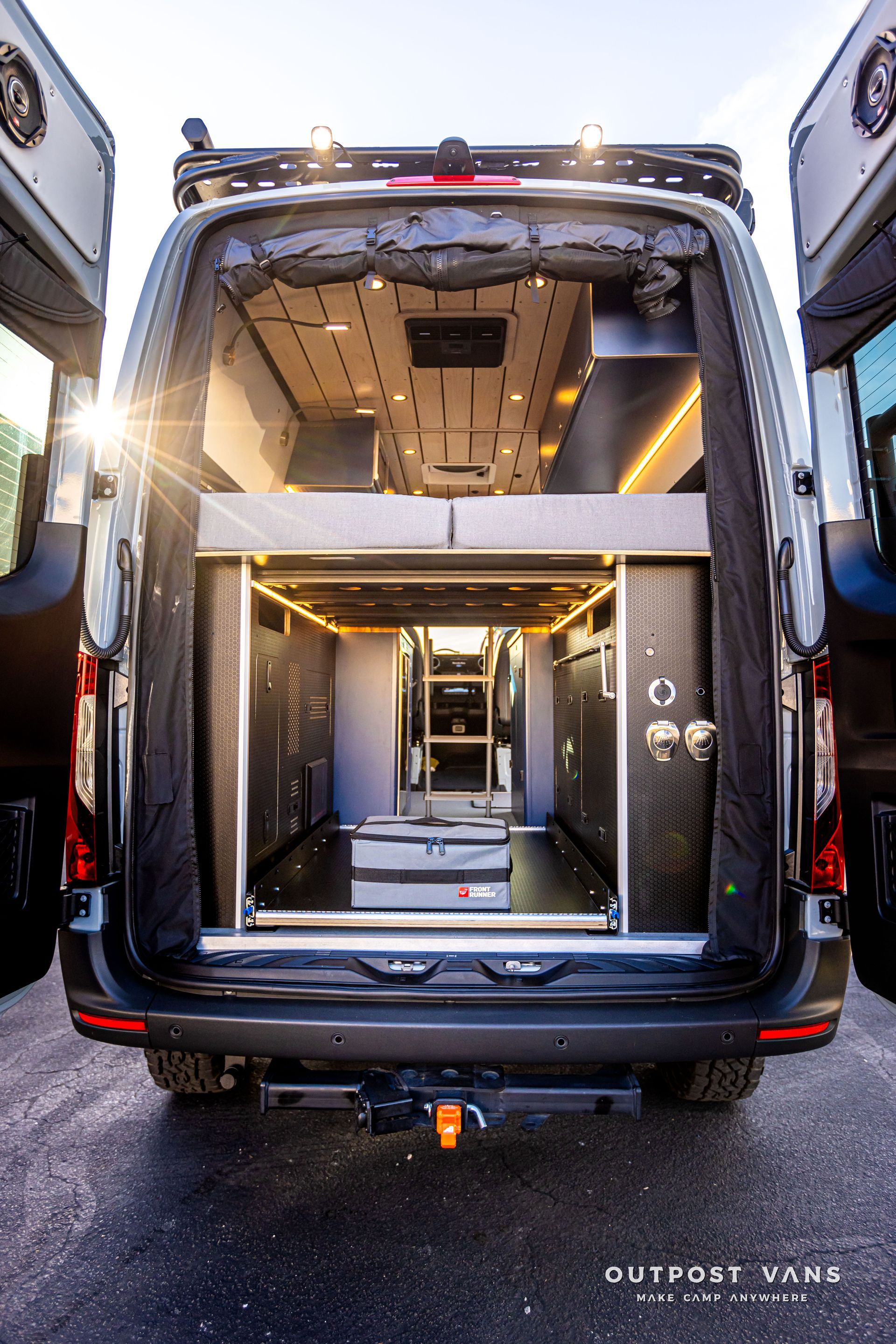 The back of a van with its doors open and a bed in the back.