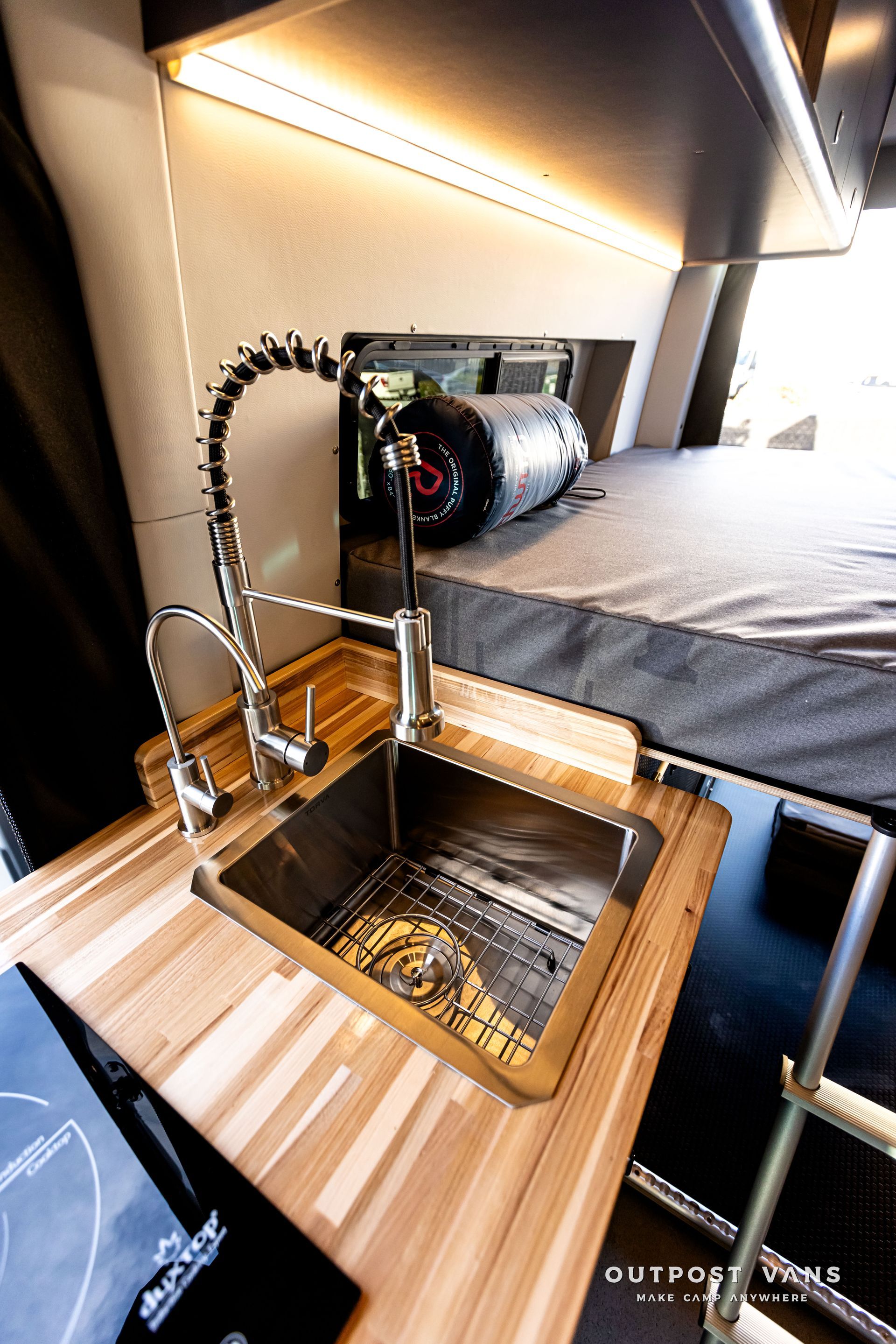 A kitchen with a sink and a bed in the background.