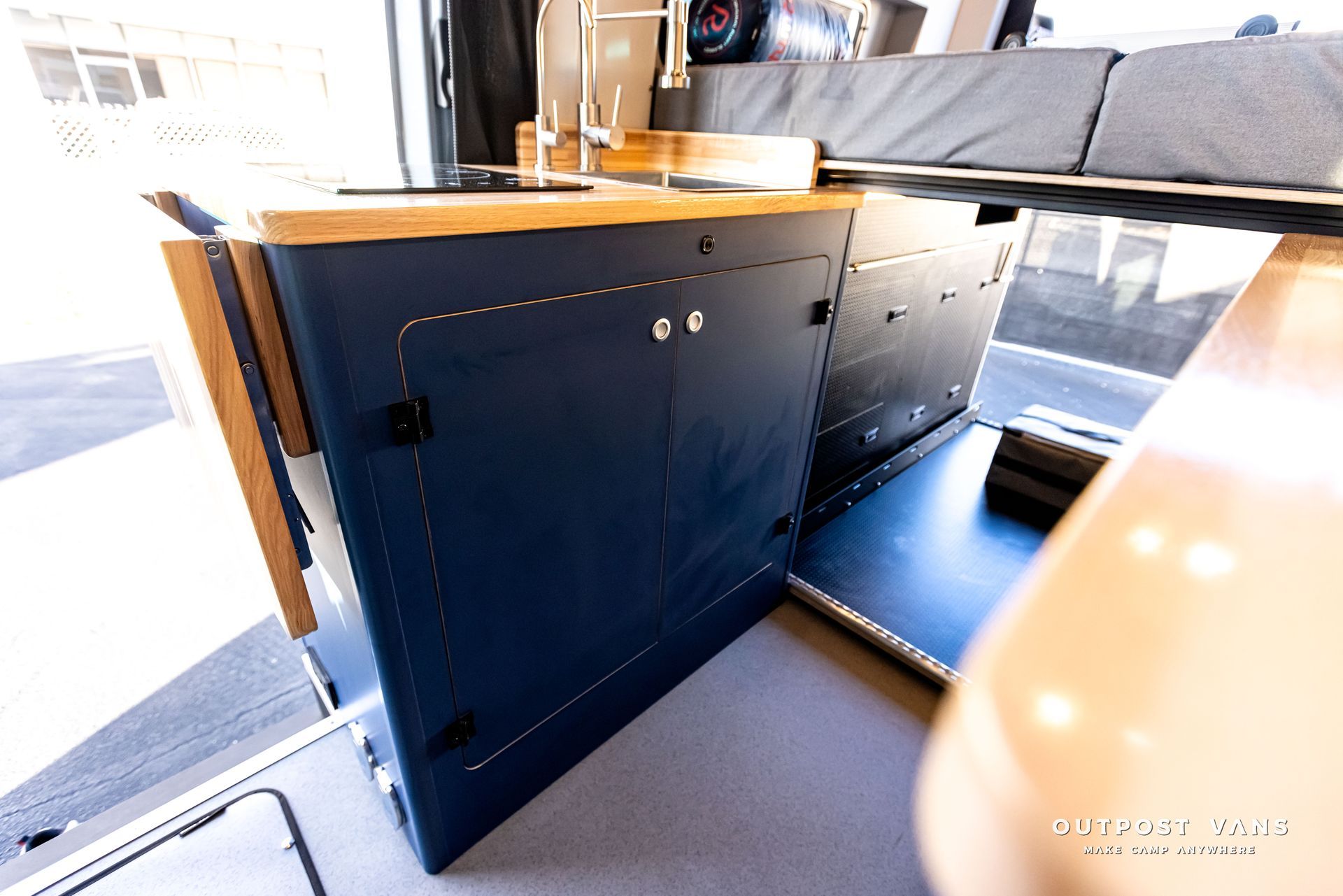 A kitchen in a van with blue cabinets and wooden counter tops.