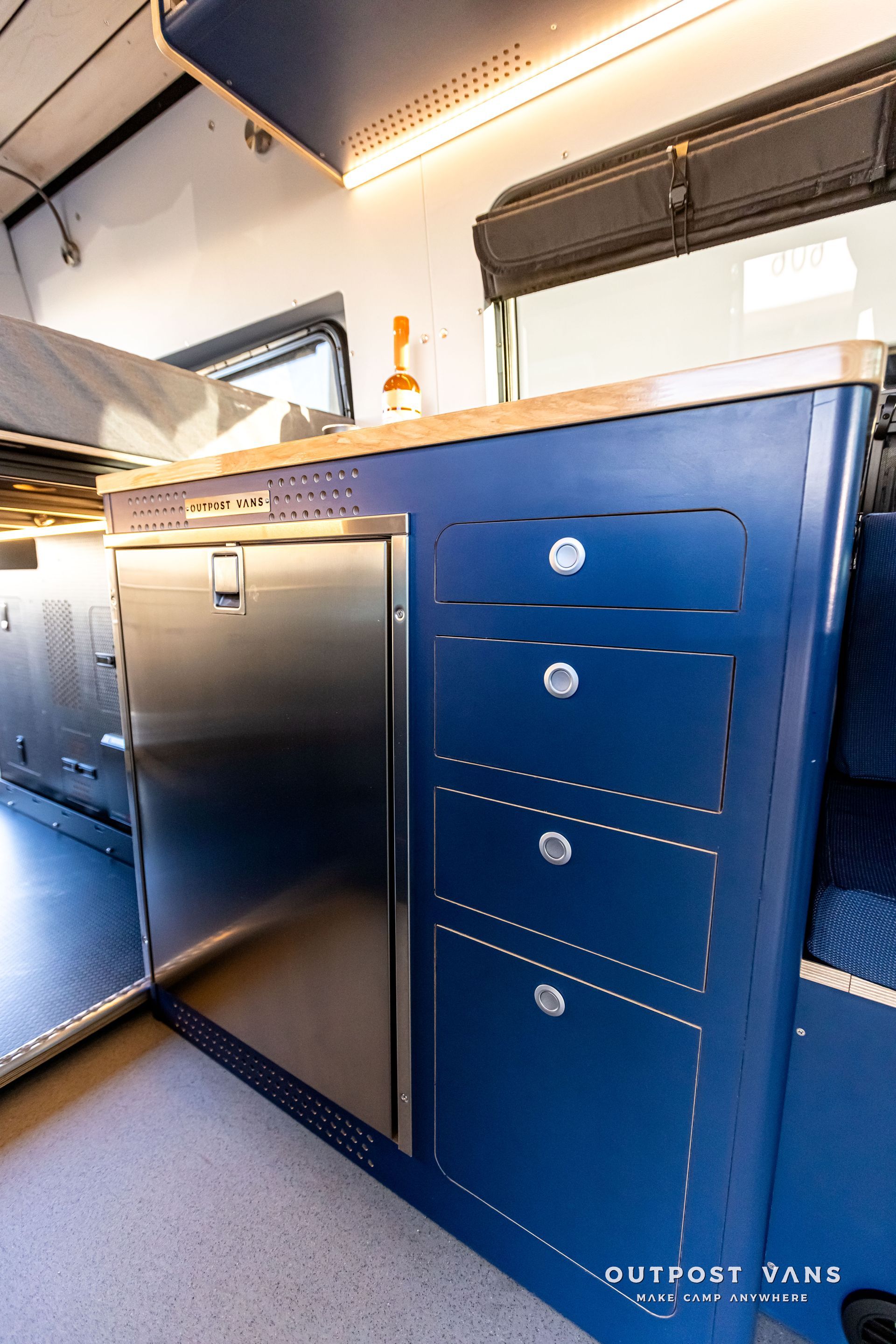 A kitchen in a van with blue cabinets and a stainless steel refrigerator.