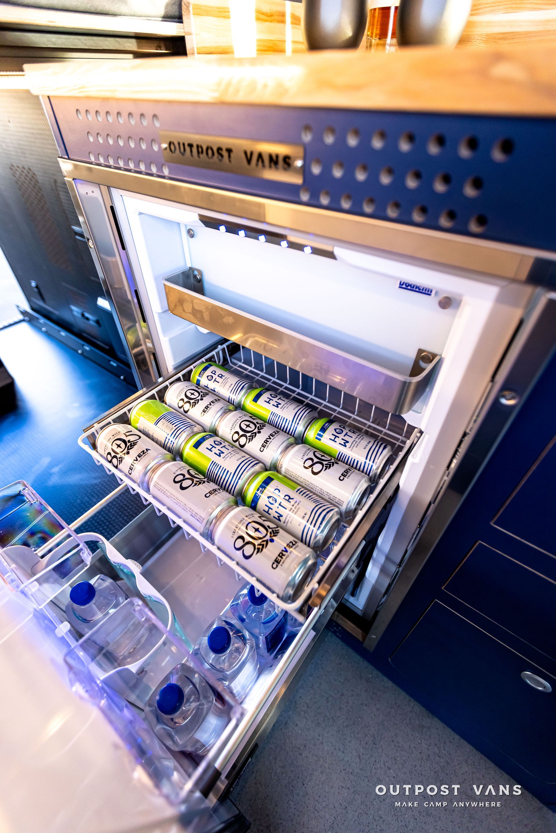 A refrigerator with a drawer full of cans and bottles.