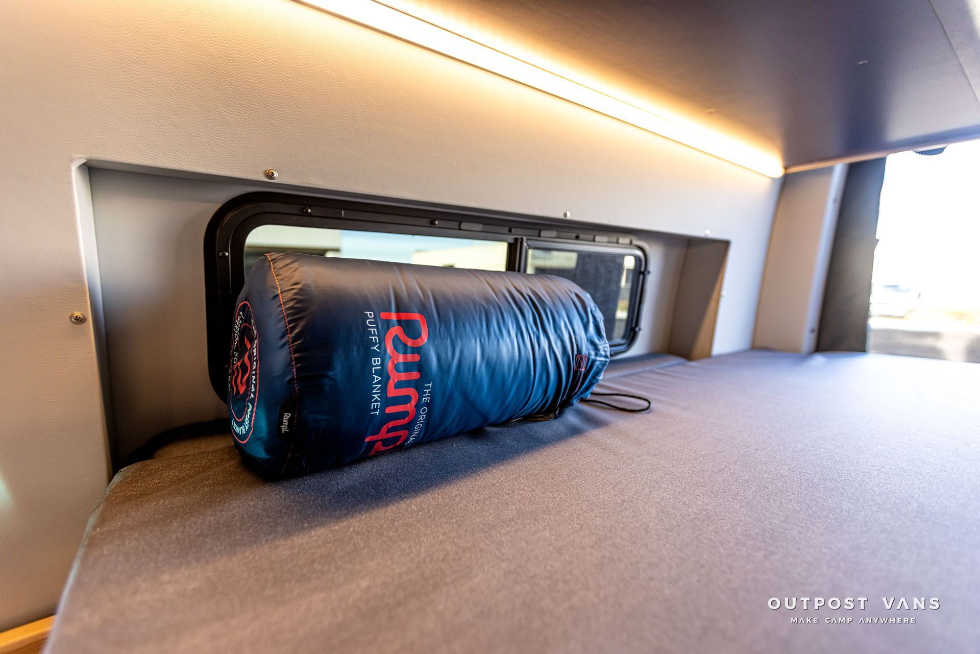 A sleeping bag is sitting on top of a bed in a van.
