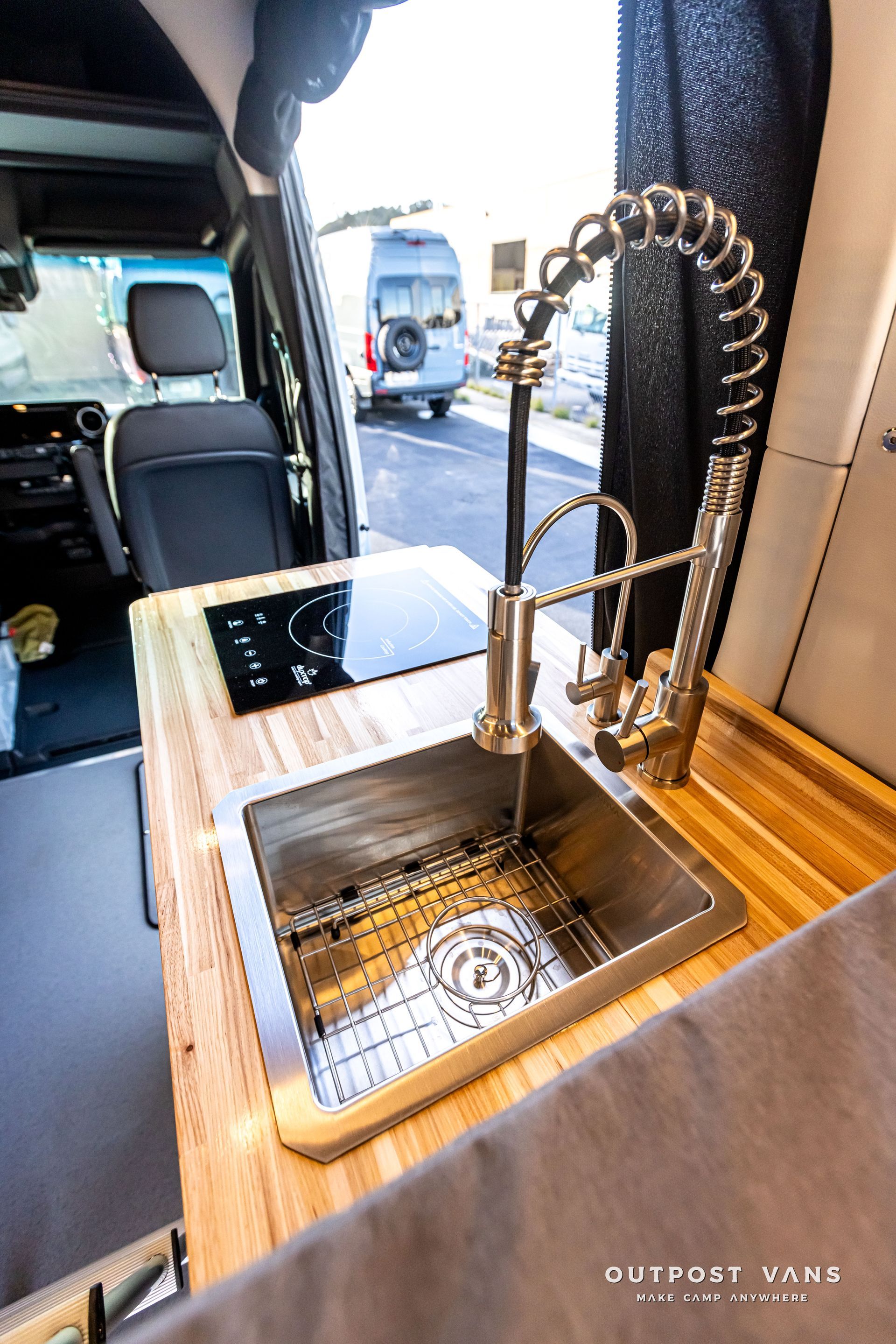A stainless steel sink is sitting on a wooden counter in a van.