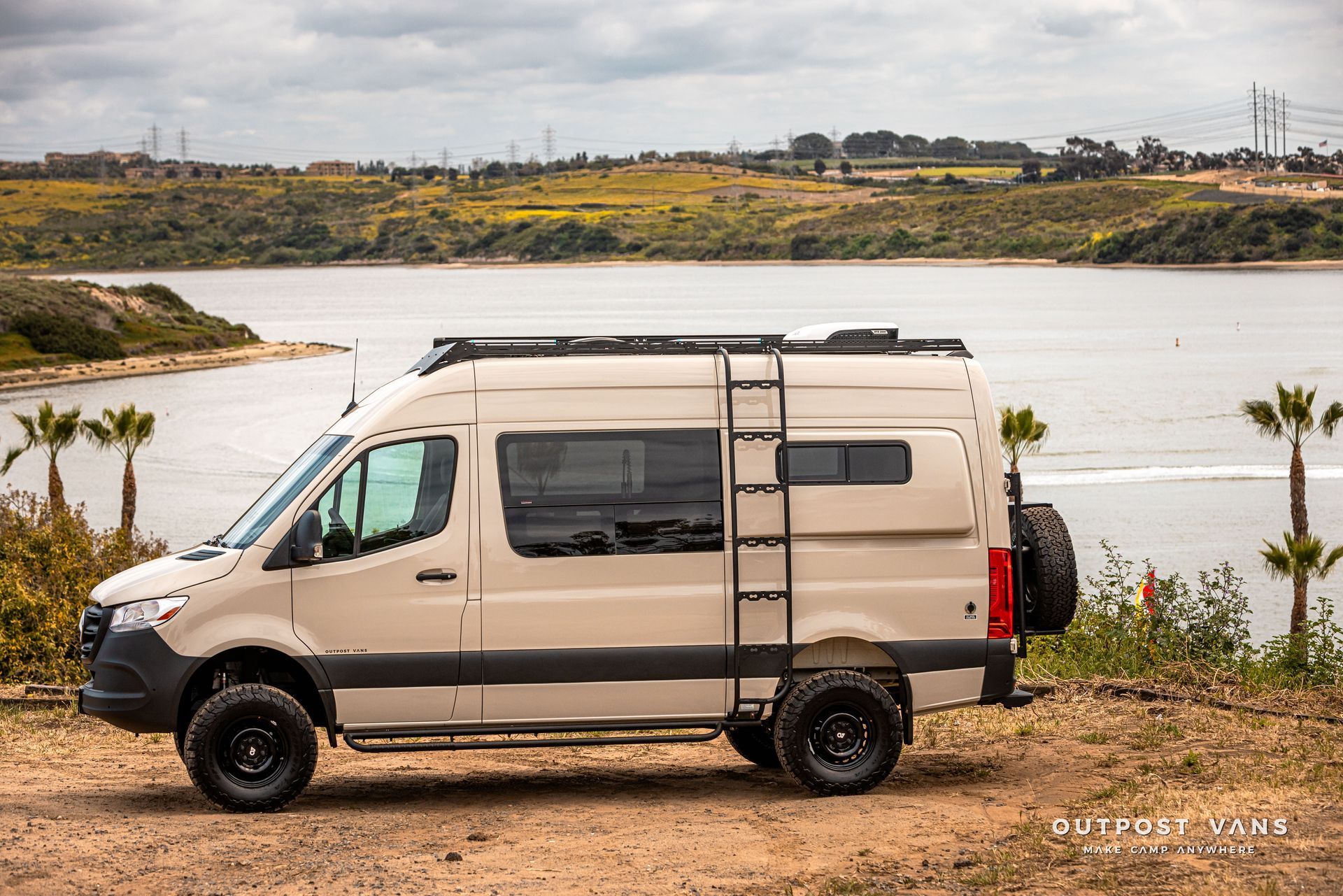 A van with a ladder on top of it is parked next to a body of water.