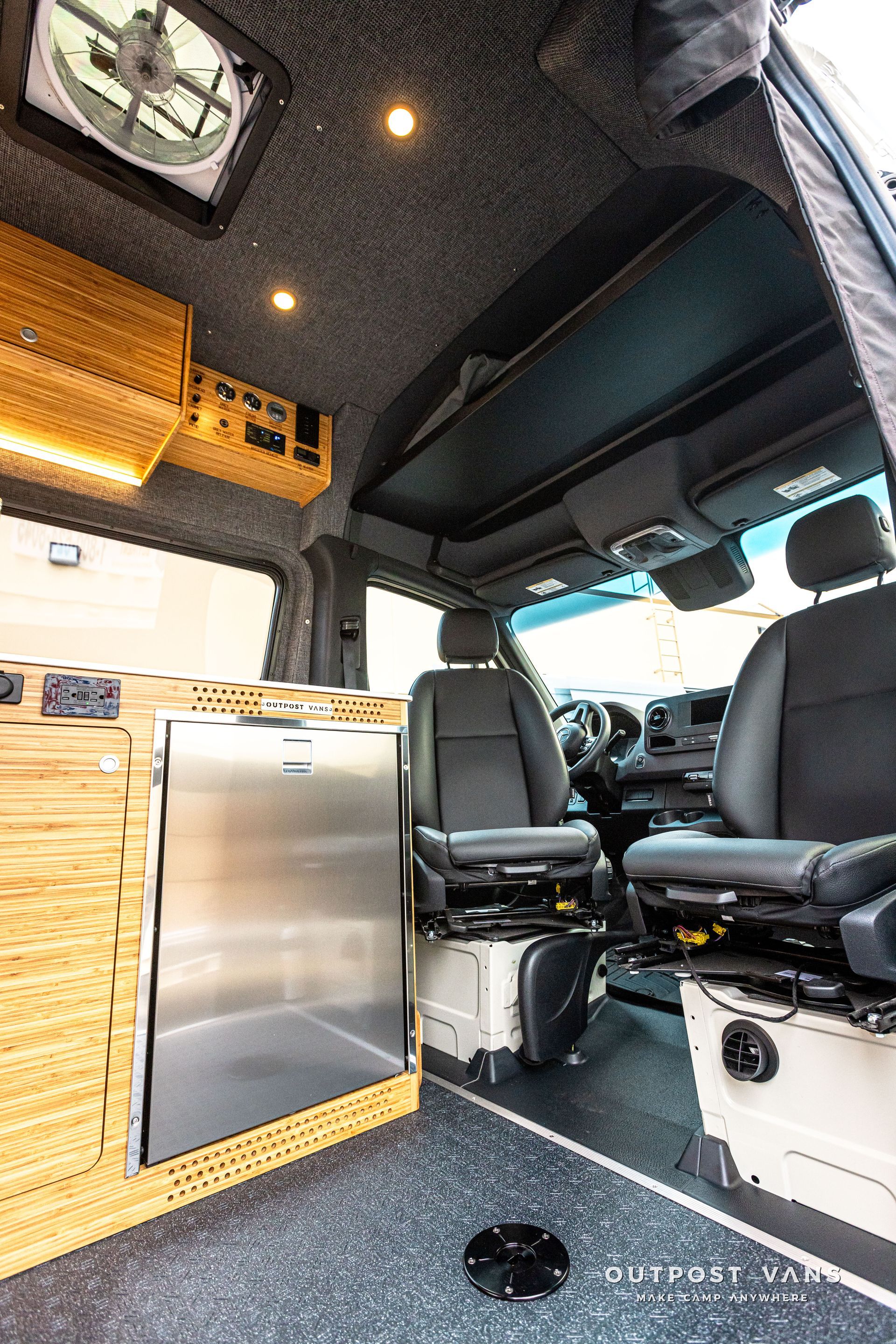 The inside of a van with a stainless steel refrigerator and a fan on the ceiling.
