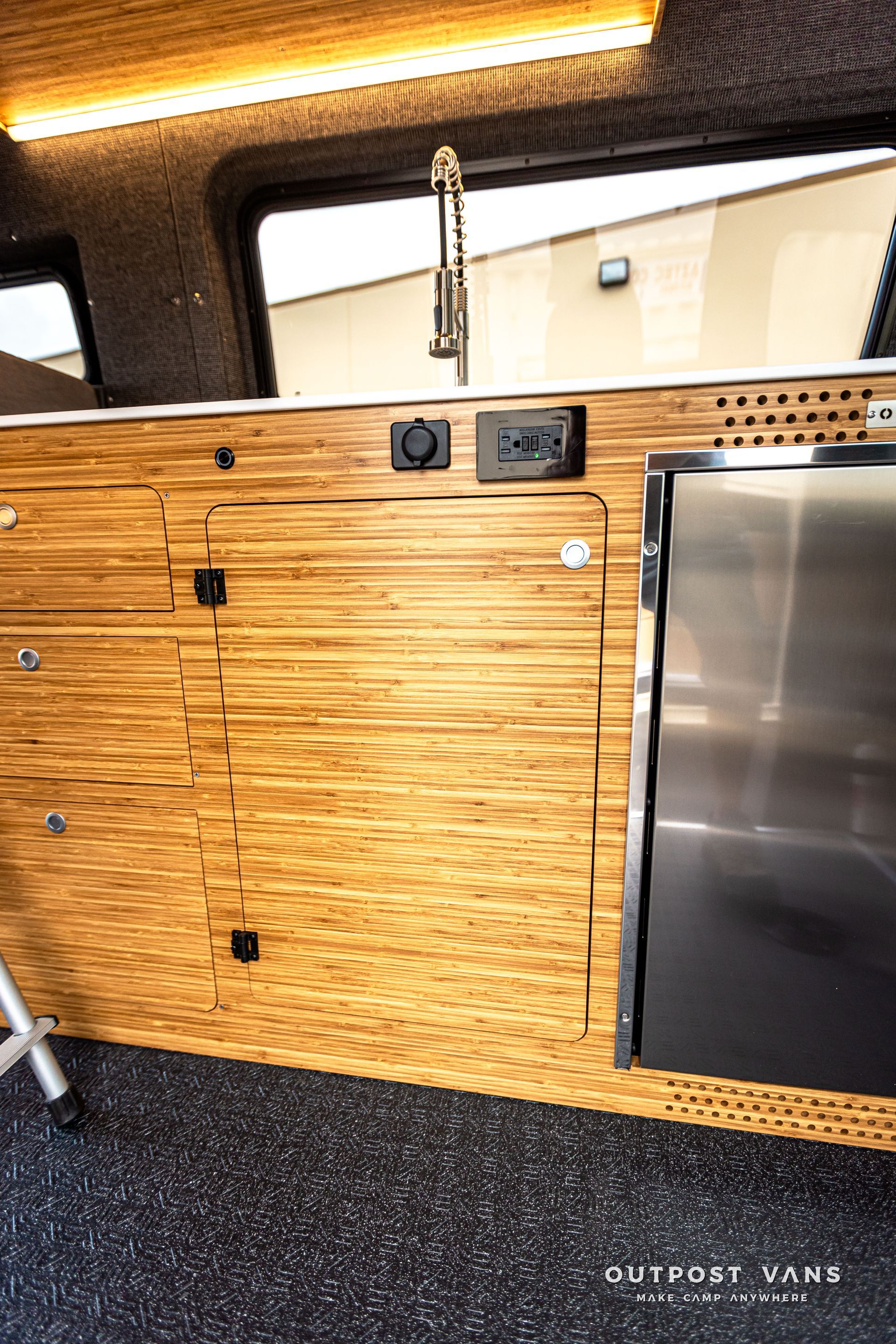 A kitchen in a van with wooden cabinets and a stainless steel refrigerator.