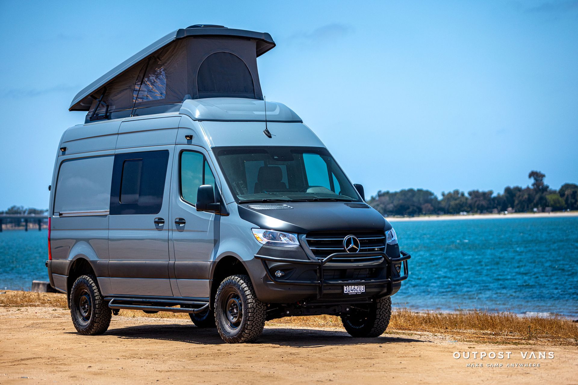 A van with a pop up roof is parked on the beach near the water.
