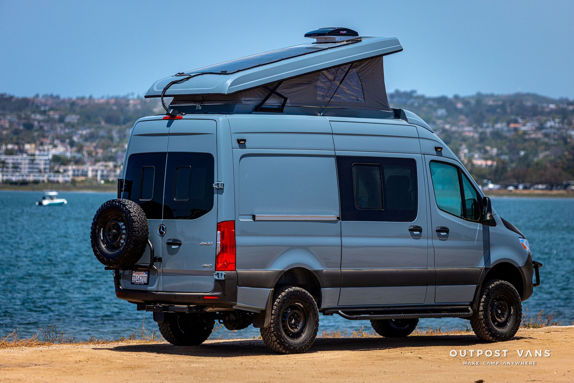 A van with a pop up roof is parked on the beach near the water.