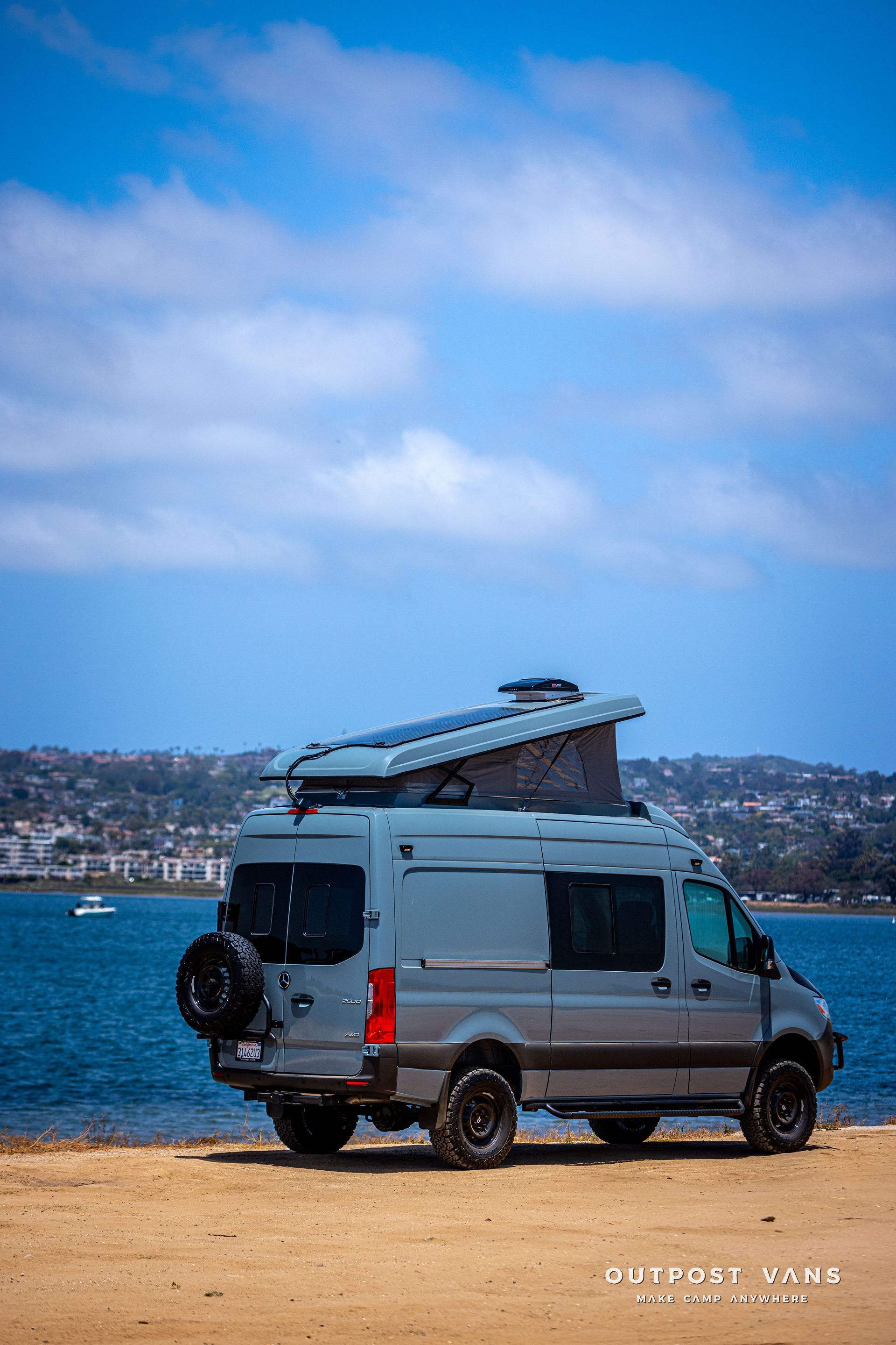 A van is parked on a sandy beach next to a body of water.