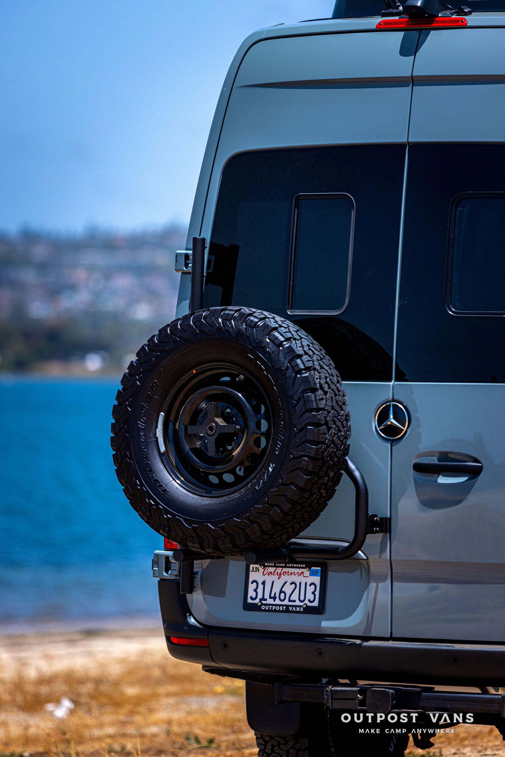 A van with a spare tire attached to the back of it is parked on the beach.