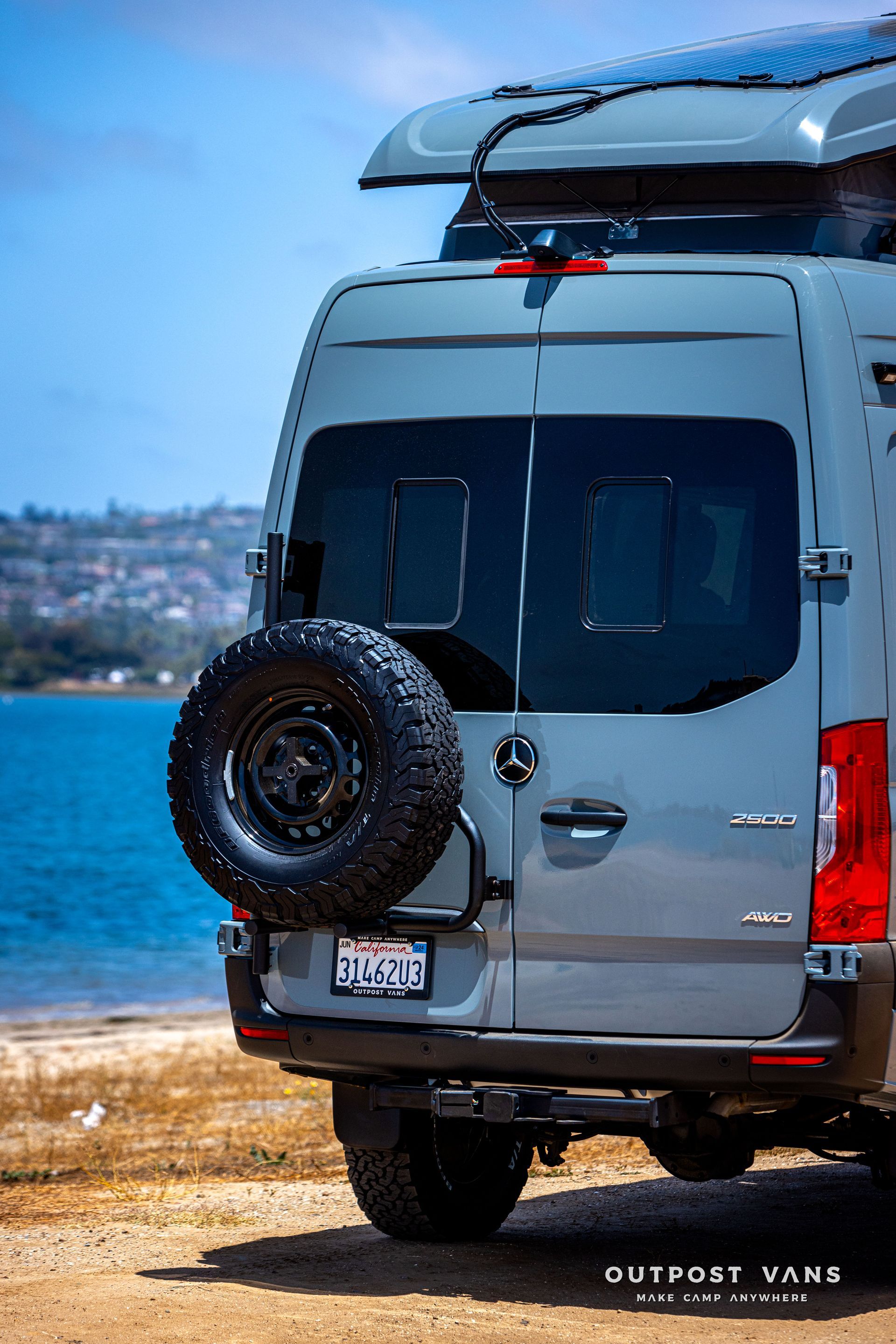A gray van is parked on the beach next to the ocean.