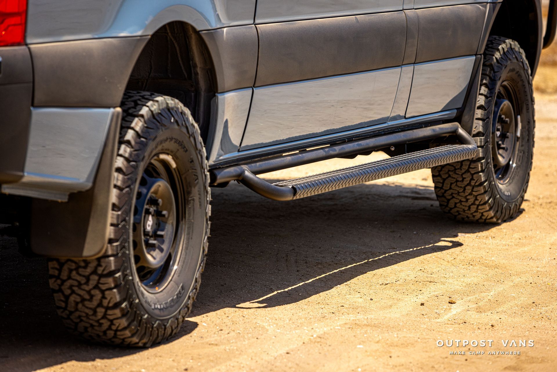 A close up of a truck 's tires and side steps on a dirt road.