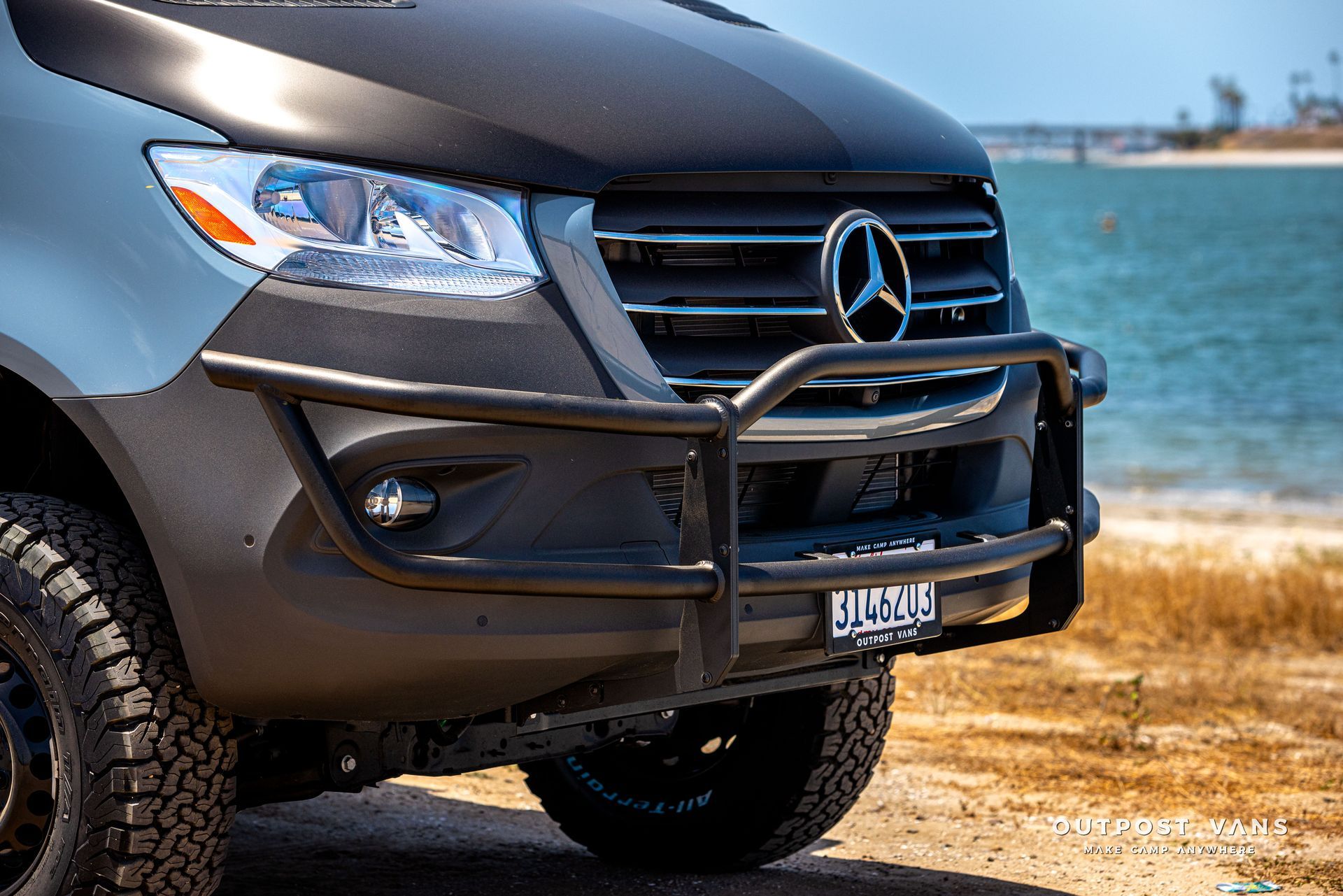 A mercedes sprinter van is parked on the beach next to the ocean.