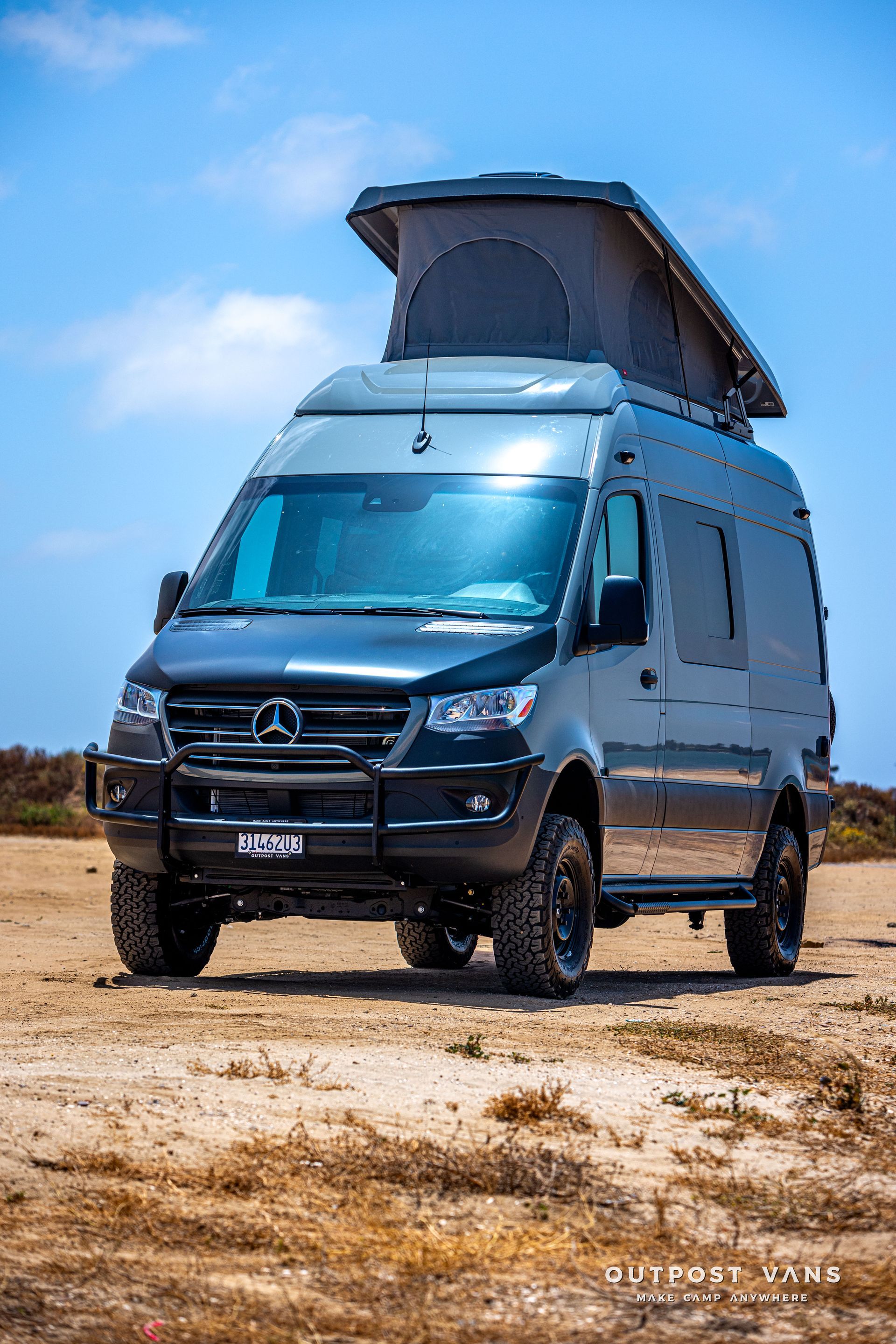 A black van with a pop up roof is parked in a dirt field.