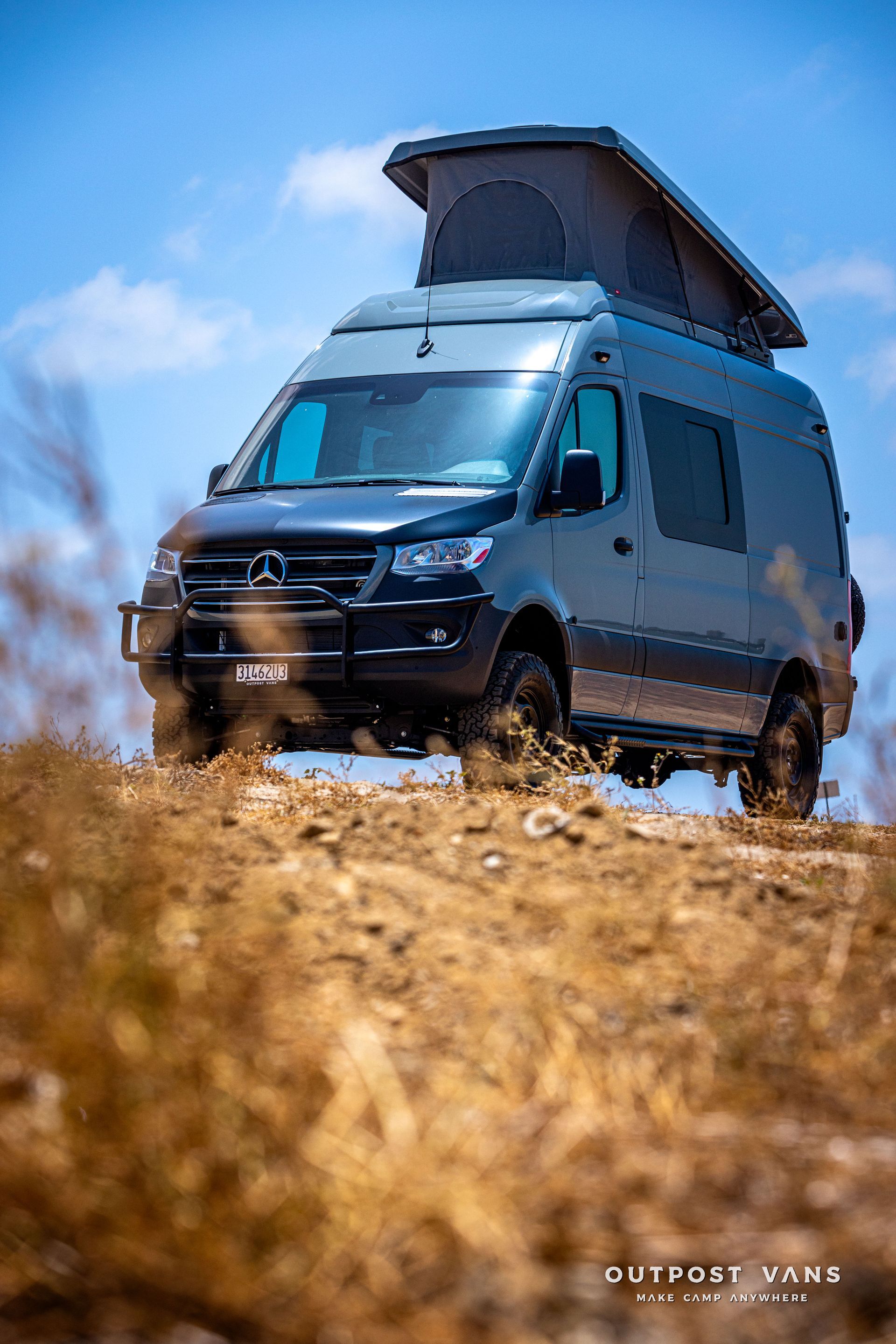 A van with a pop up roof is driving down a dirt road.