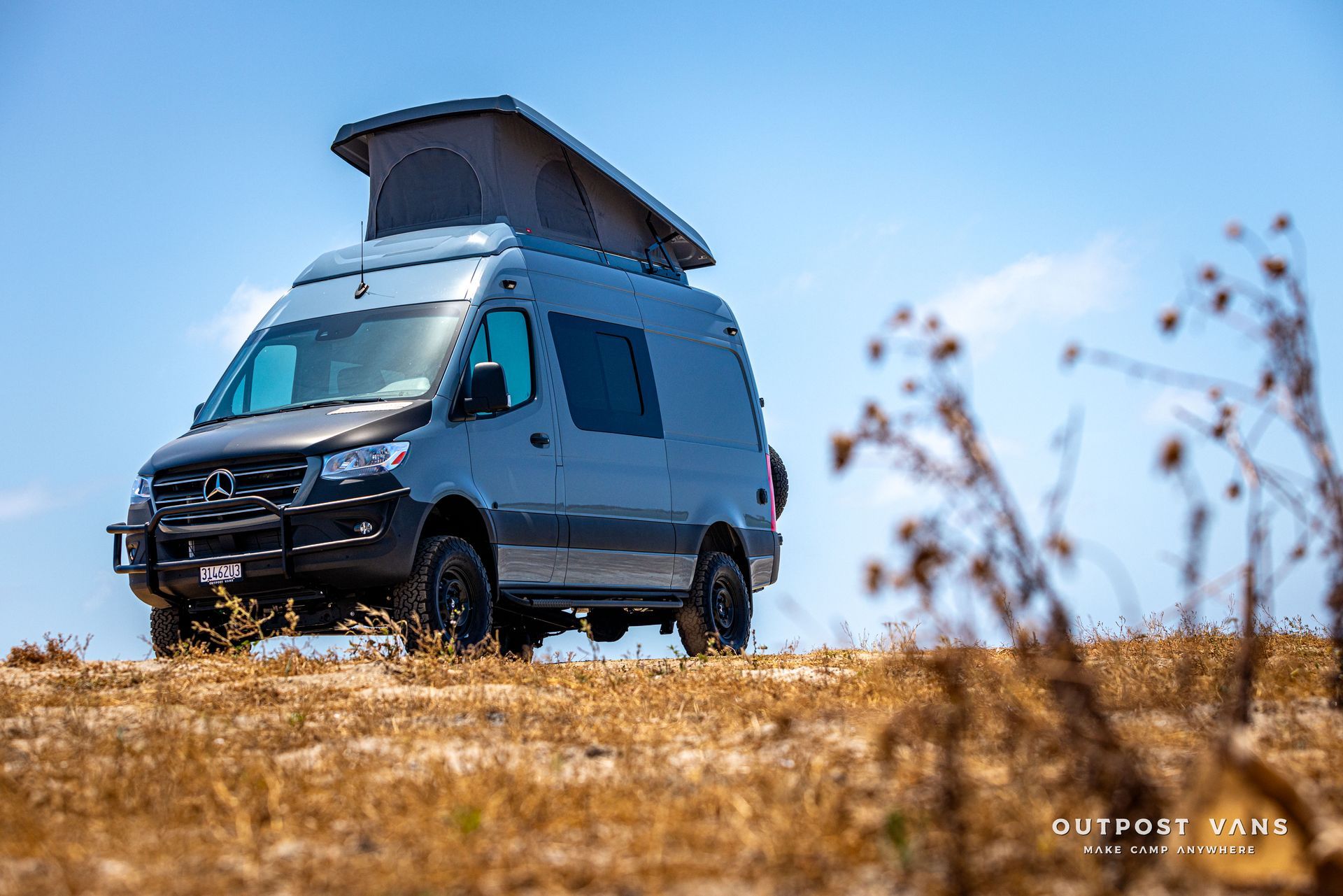 A van with a pop up roof is parked on top of a dry grassy hill.