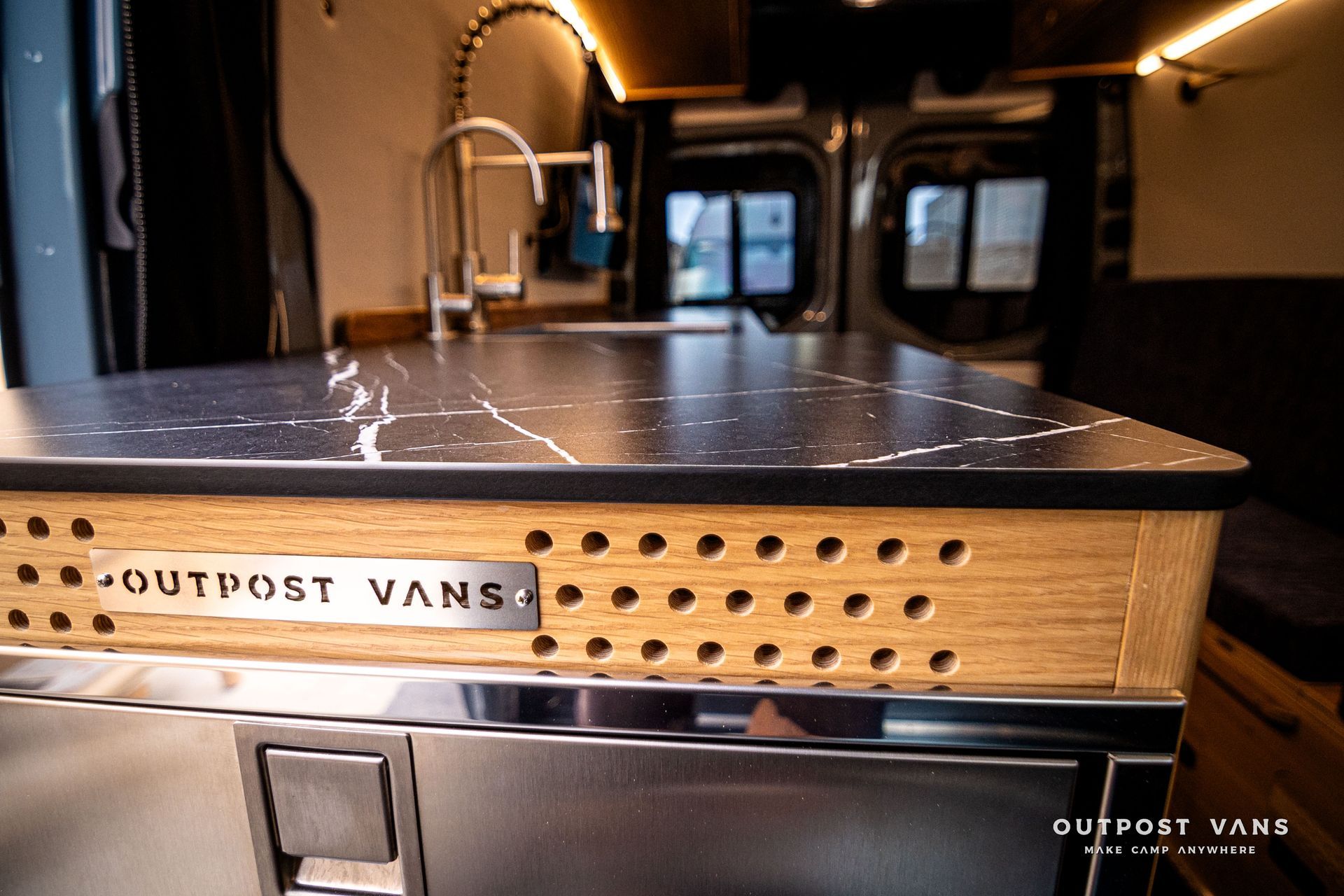 A kitchen in a van with a marble counter top and a stainless steel refrigerator.