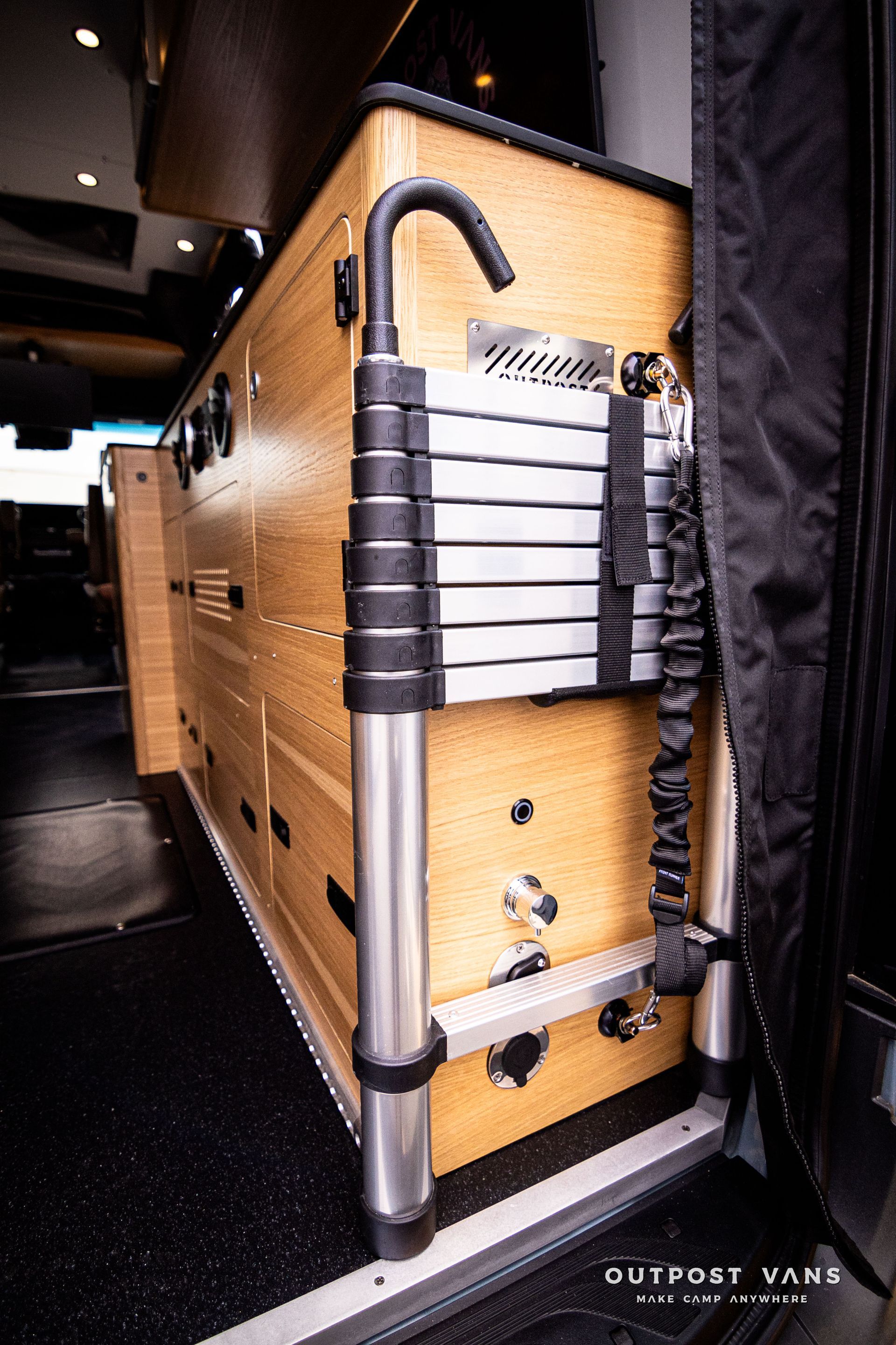 A ladder is attached to a wooden cabinet in a van.