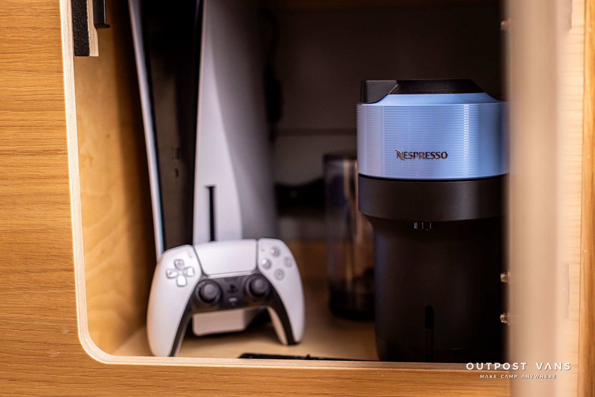 A ps5 console is sitting on top of a wooden shelf next to a coffee maker.
