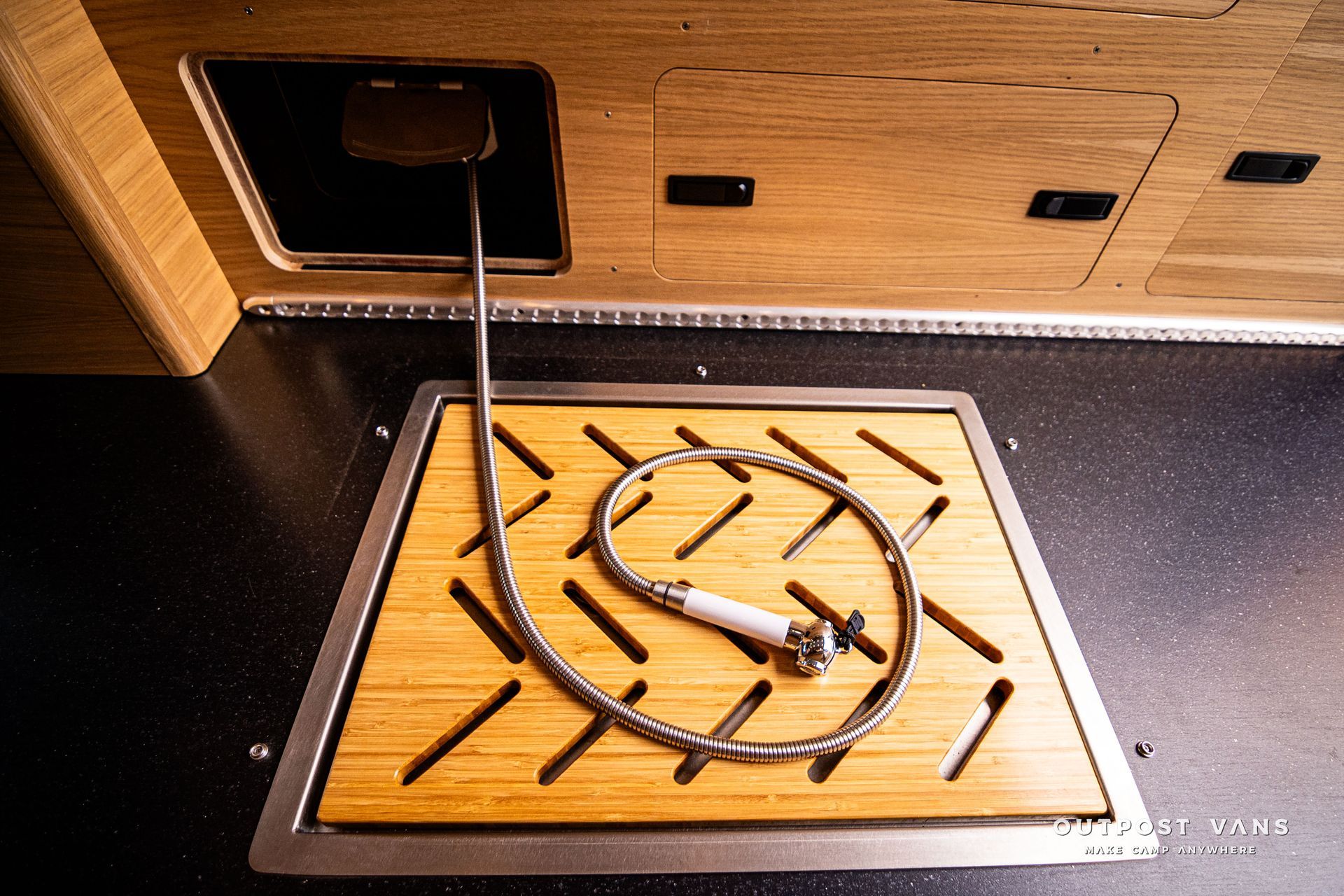 A shower head is sitting on a wooden tray in a kitchen.