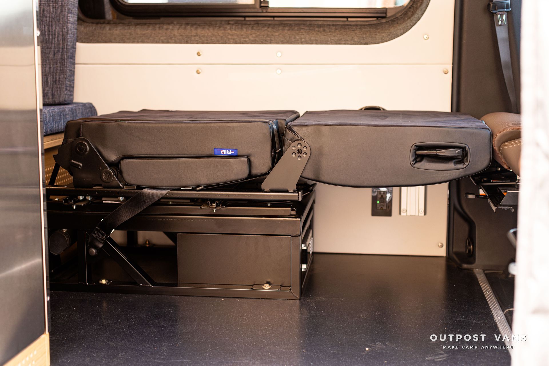 The back seat of a van is folded up and ready to be used as a bed.