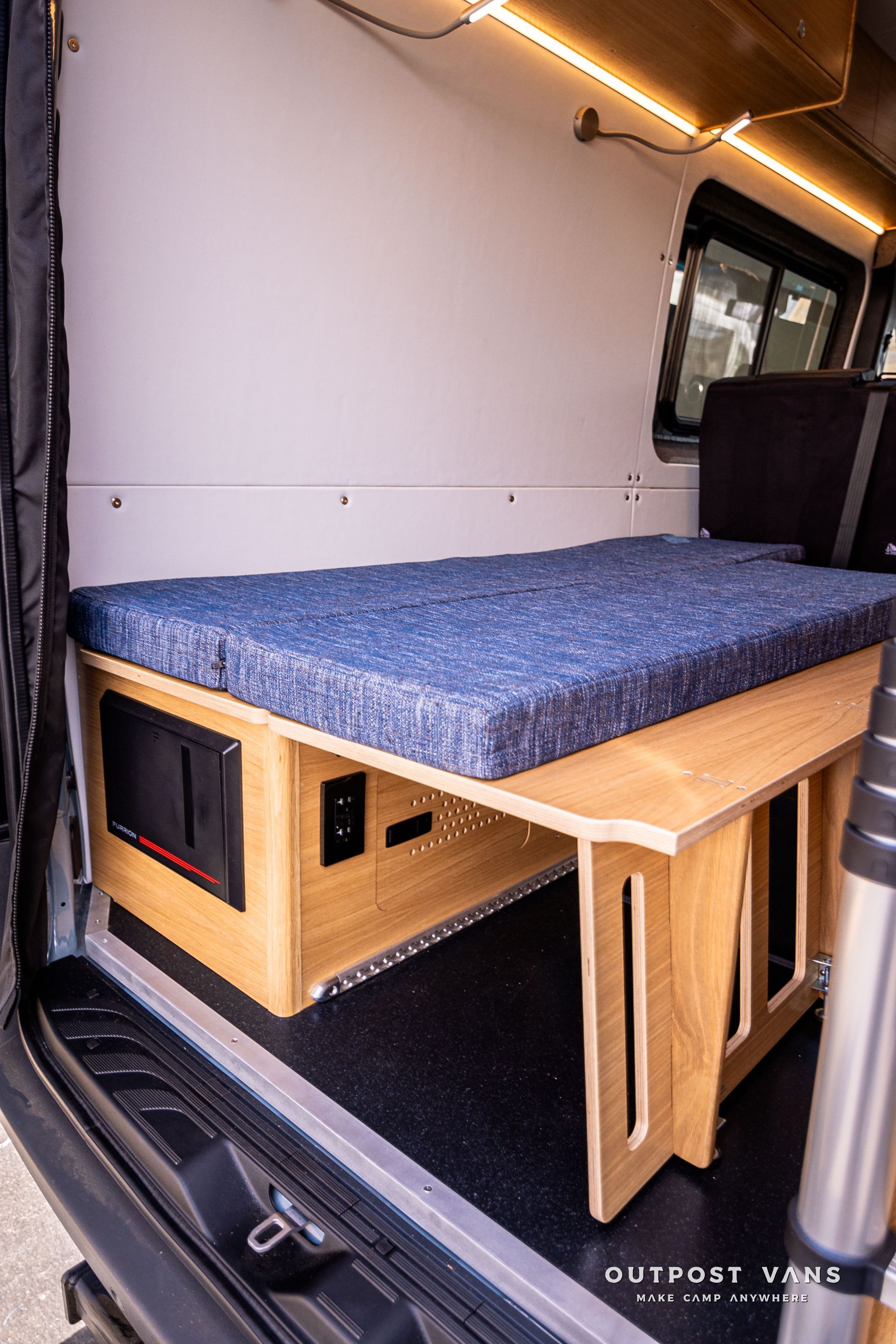 A bed in the back of a van with a blue mattress.