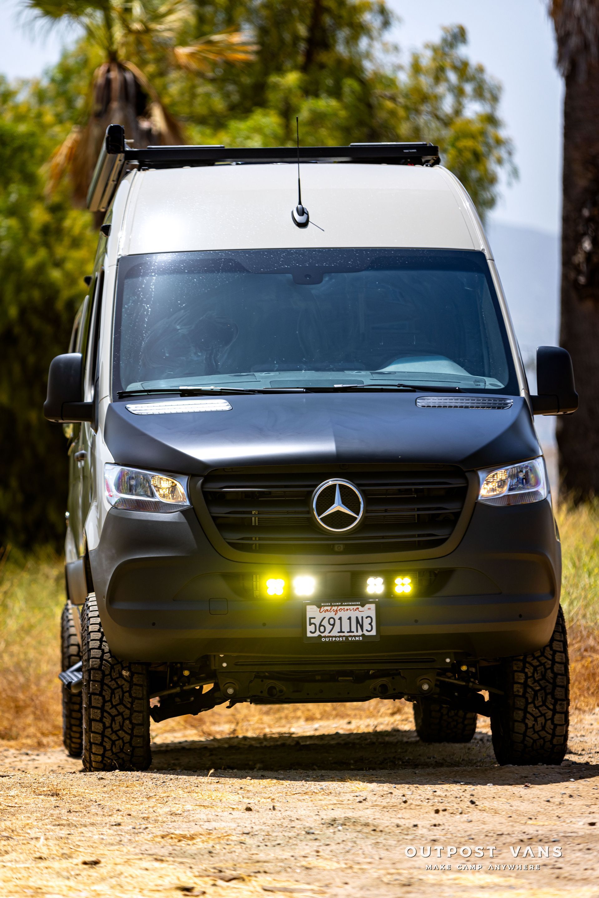 A black and white mercedes sprinter van is parked on a dirt road.
