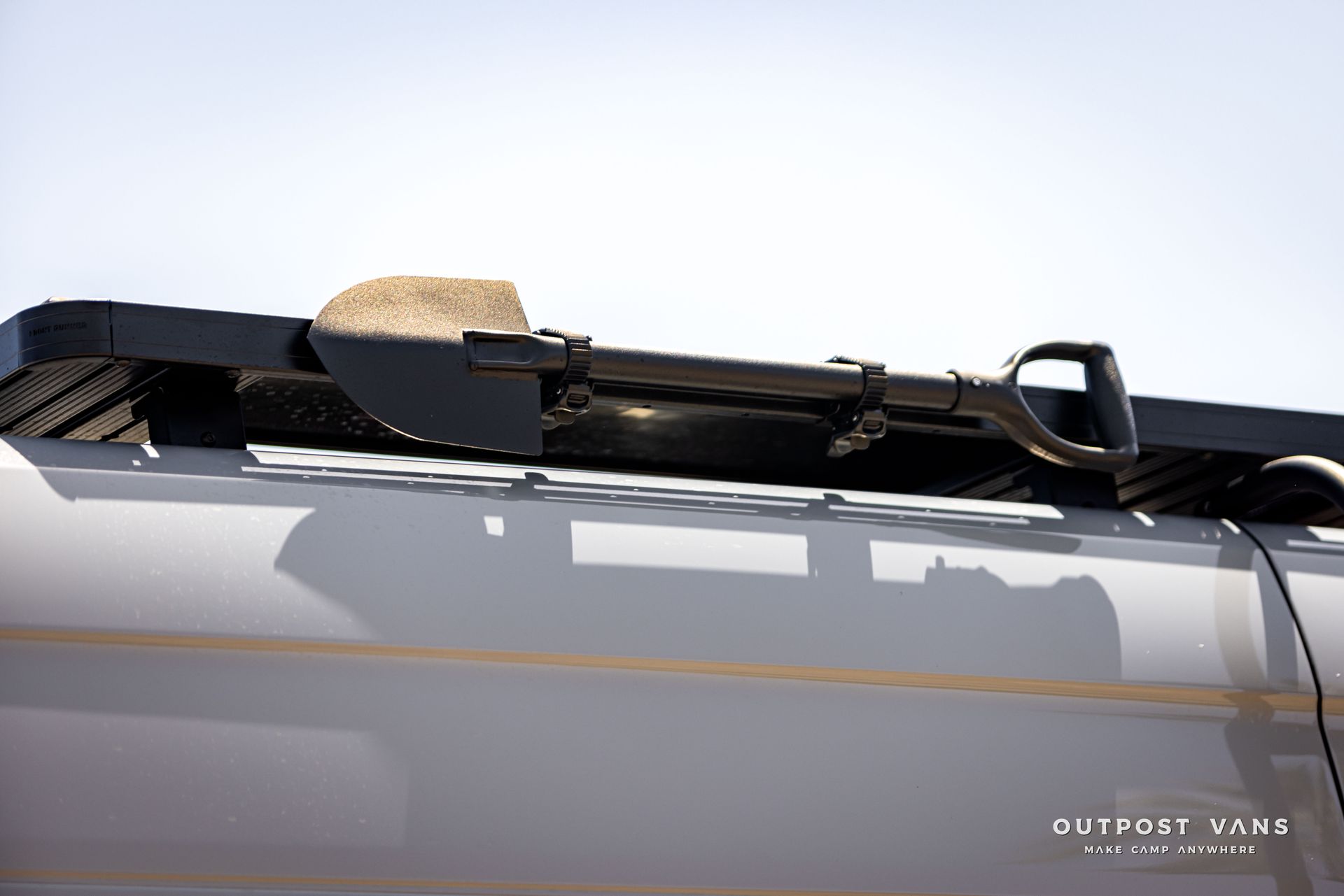 A shovel is attached to the roof of a vehicle.