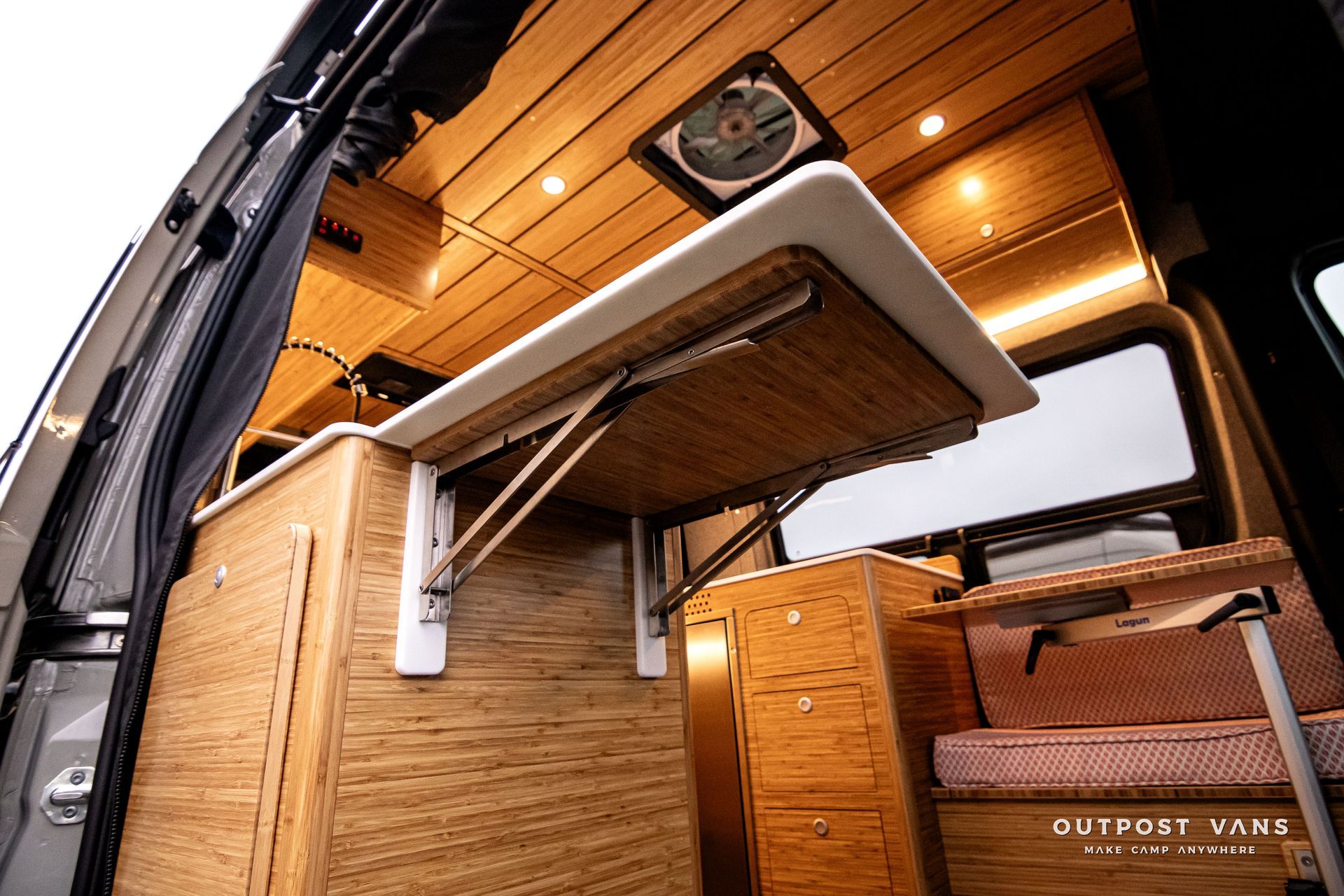 A camper van with a folding table and a fan on the ceiling.