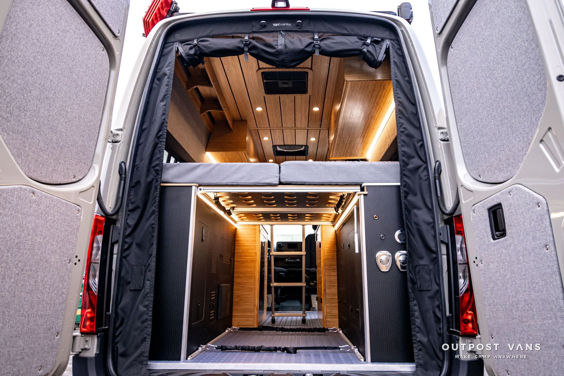 The back of a van with its doors open and a bed in the back.