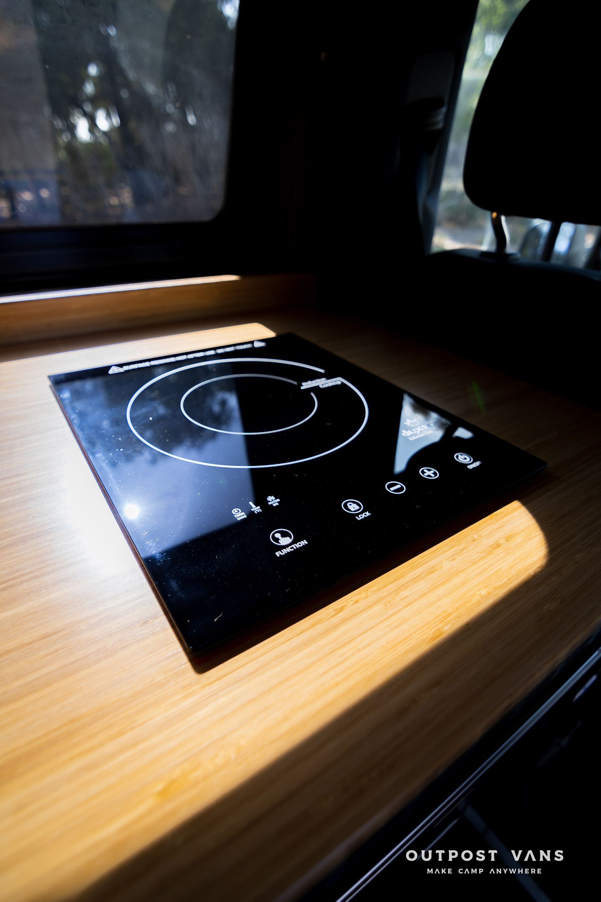 A small stove is sitting on a wooden table in a van.