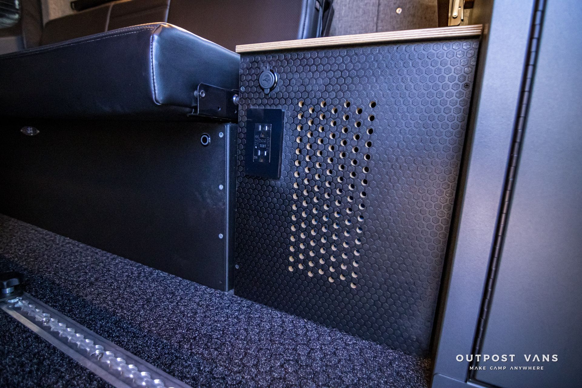 A black box with holes in it is sitting next to a bed.