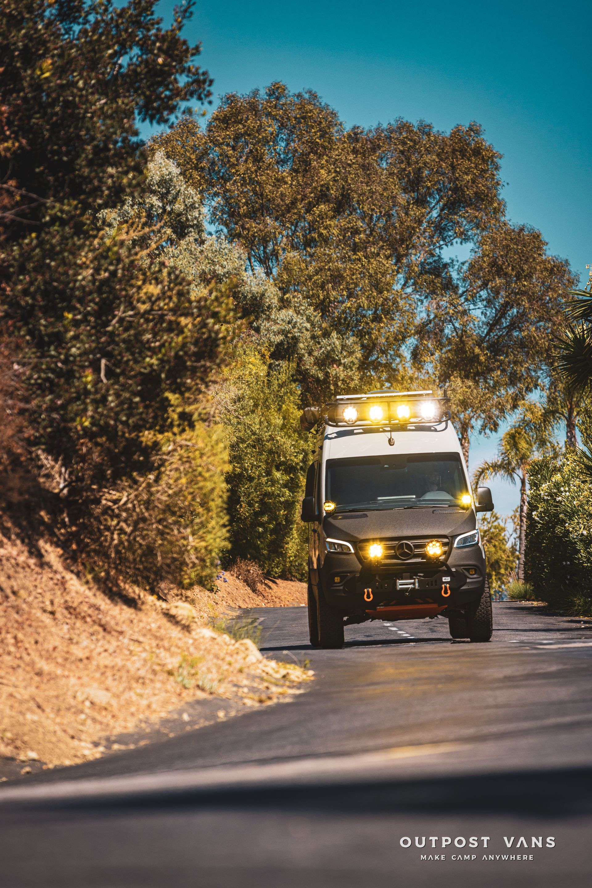 A van is driving down a road with trees in the background.