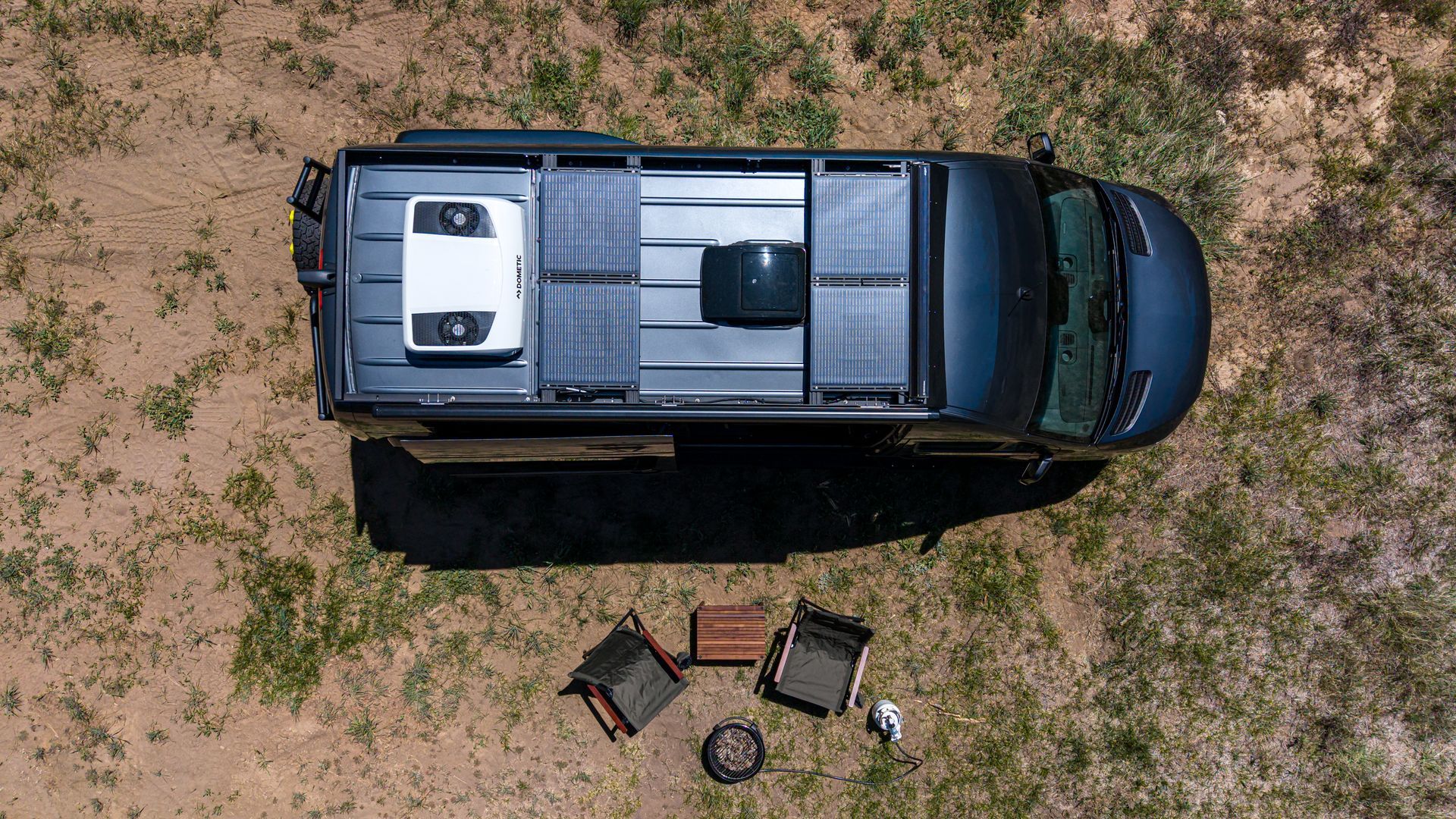 Top-down view of a black pickup truck on dirt with camping gear laid out beside it.
