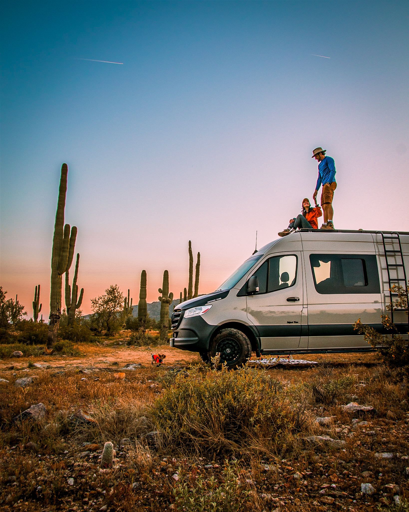 A man is standing on top of a van in the desert.