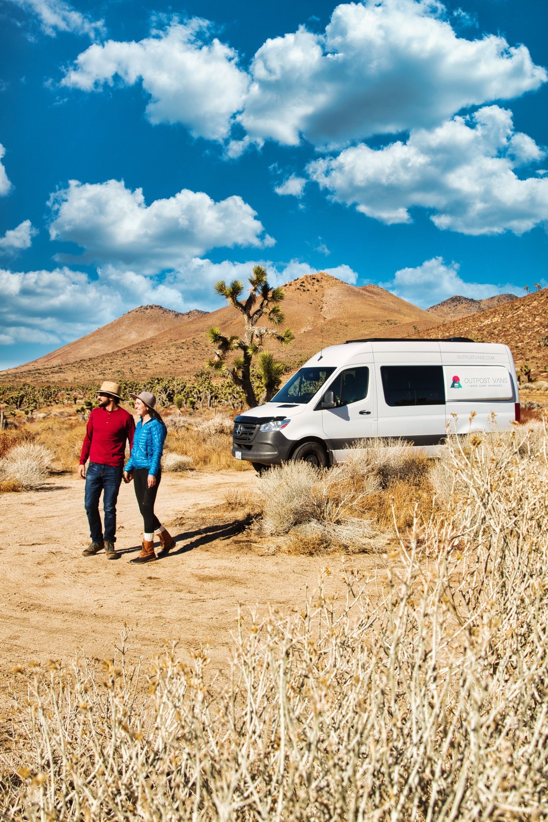 a man and woman are walking in the desert next to a van .