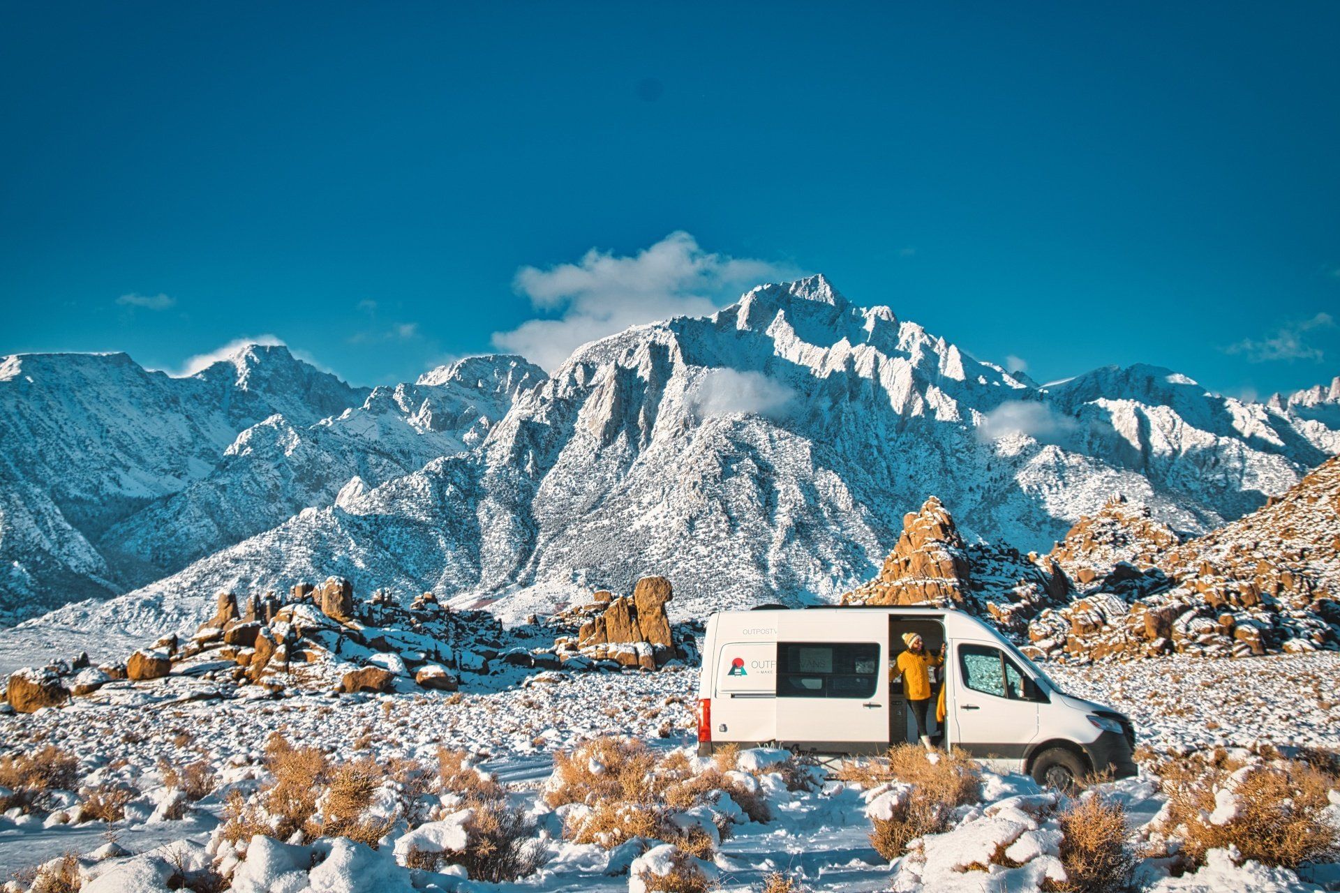 a white van is parked in the snow in front of a snowy mountain .
