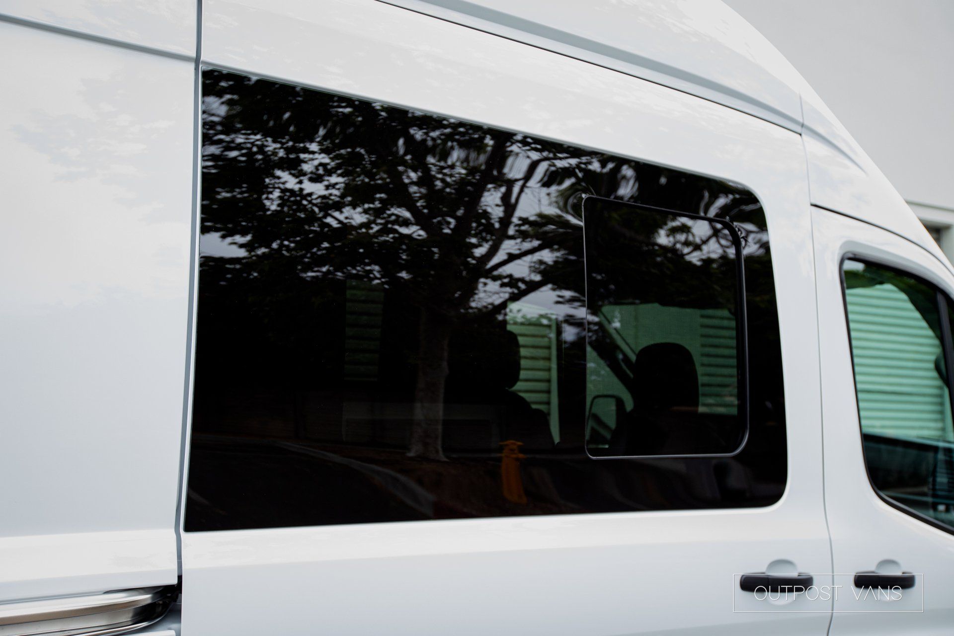 a white van with a black window is parked in a parking lot .