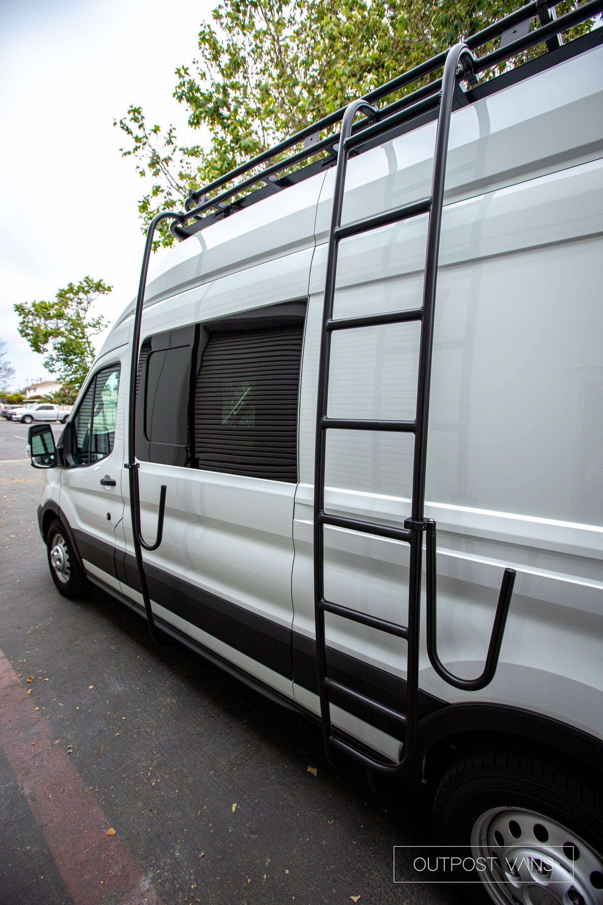 a white van with a ladder attached to the side is parked on the side of the road .