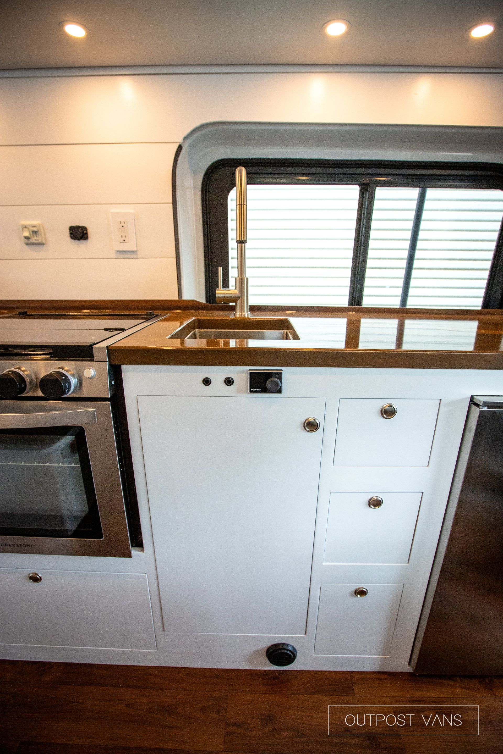 a kitchen with white cabinets , a sink , a stove , and a window .