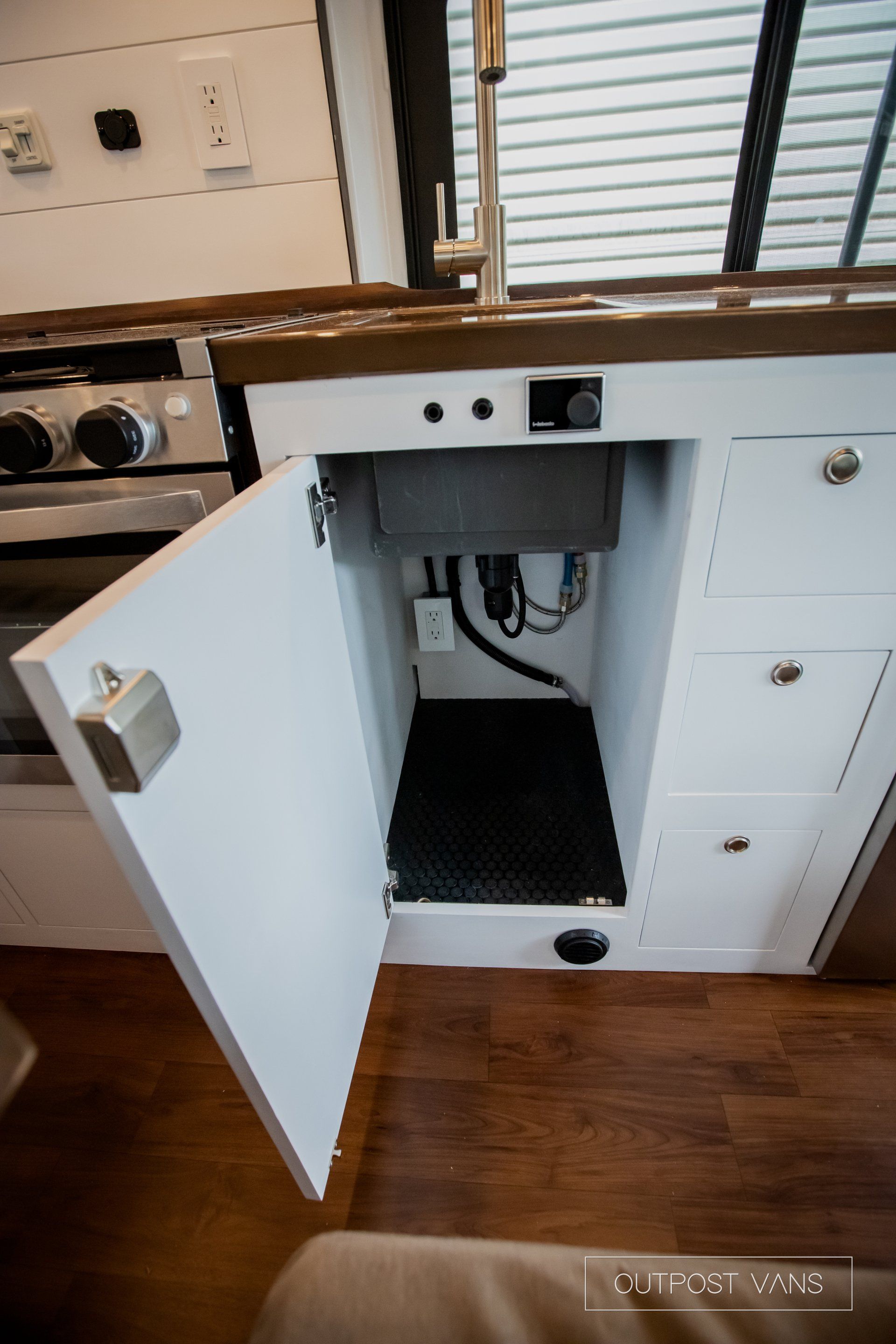 a kitchen sink is under a cabinet with the door open .