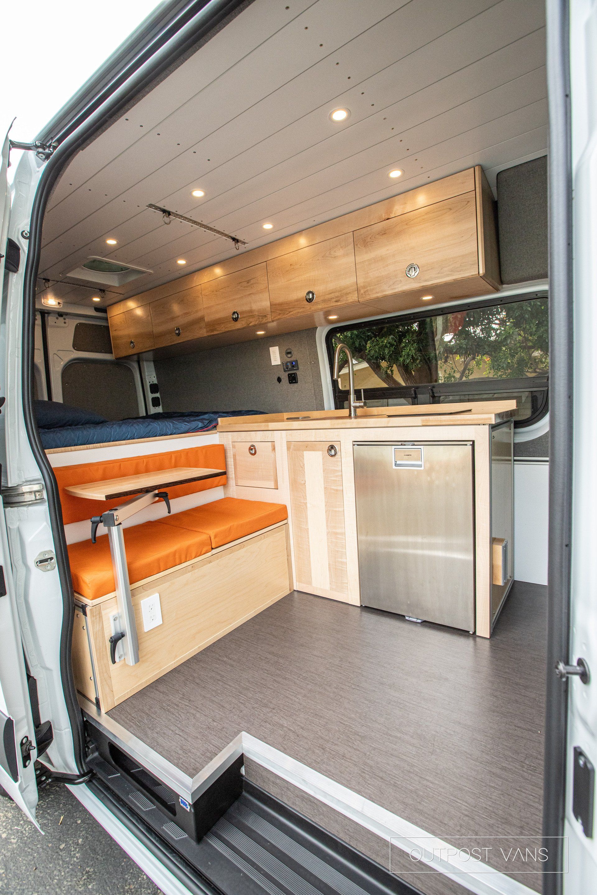 the inside of a van with wooden cabinets and a stainless steel refrigerator .