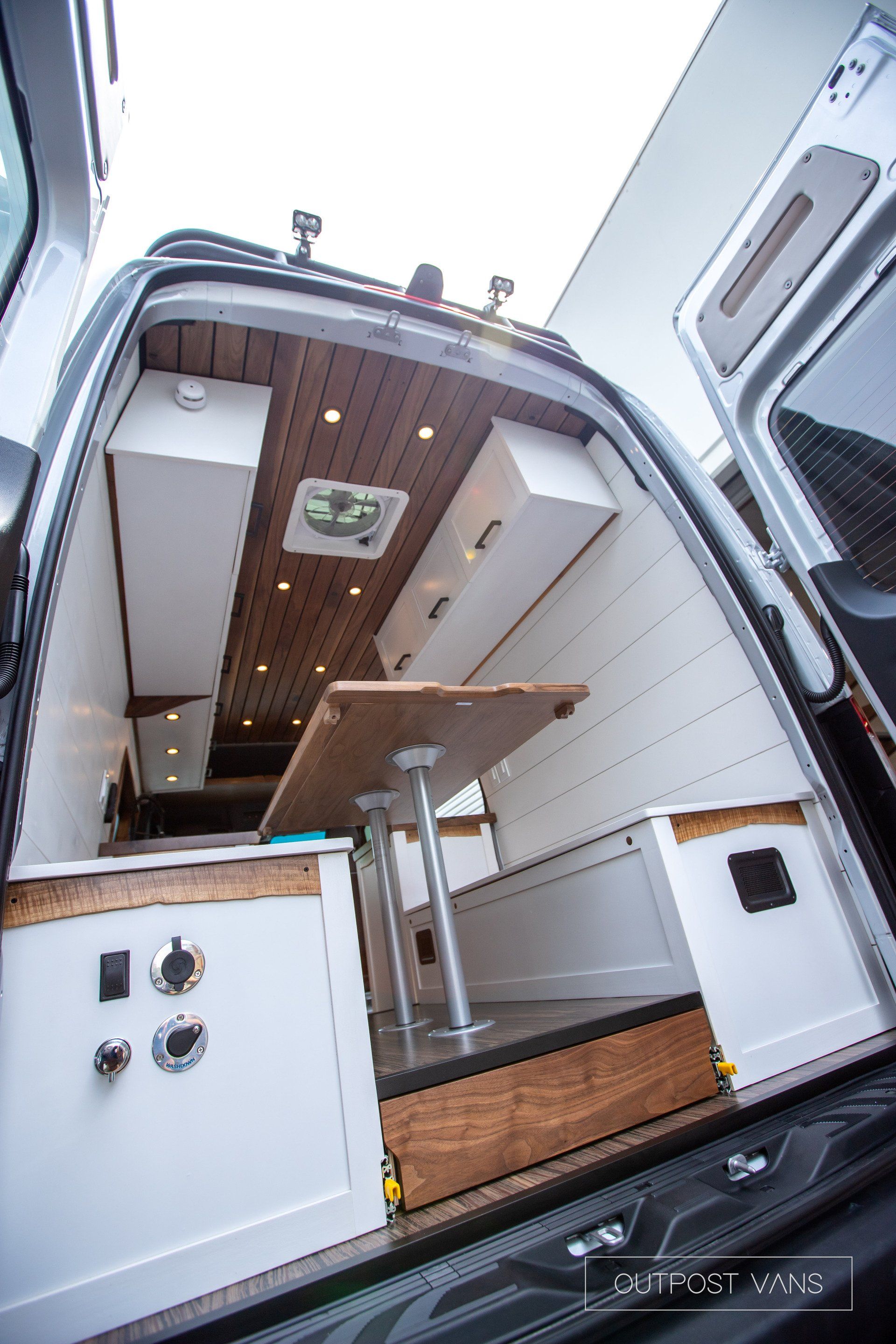 The back of a van with a table and a fan on the ceiling.