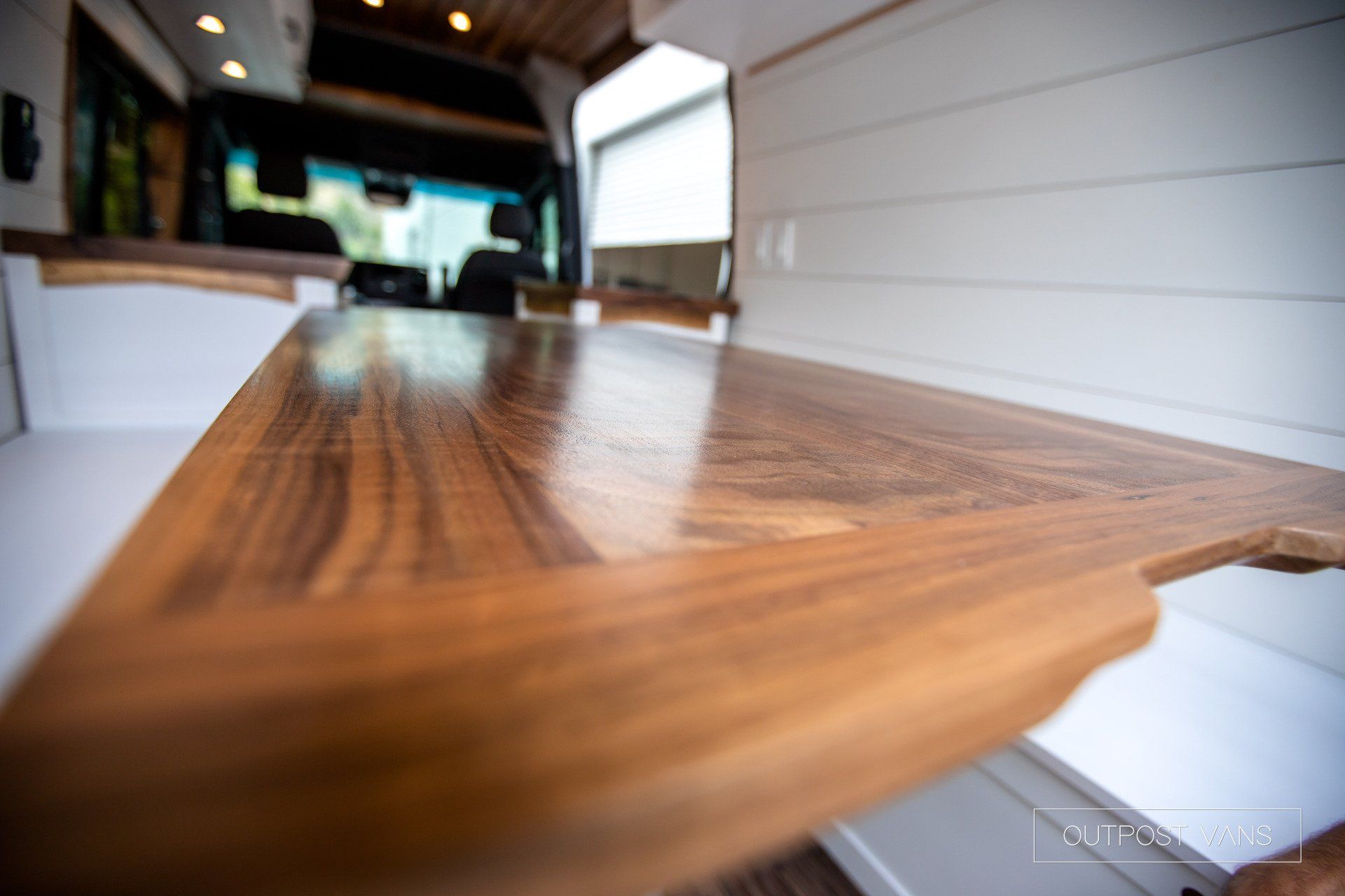A wooden table in a van with a car in the background