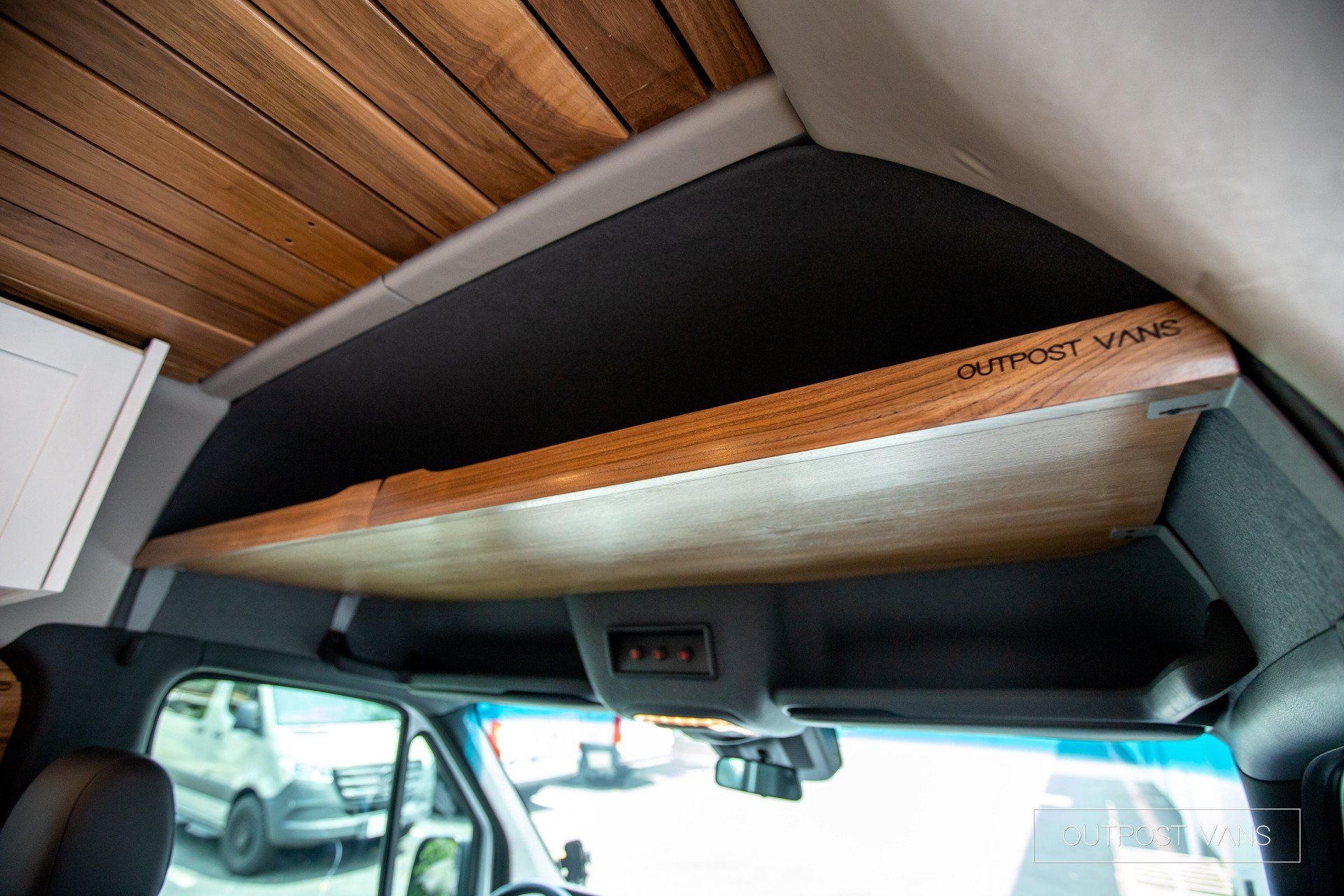 There is a wooden shelf in the ceiling of a van.