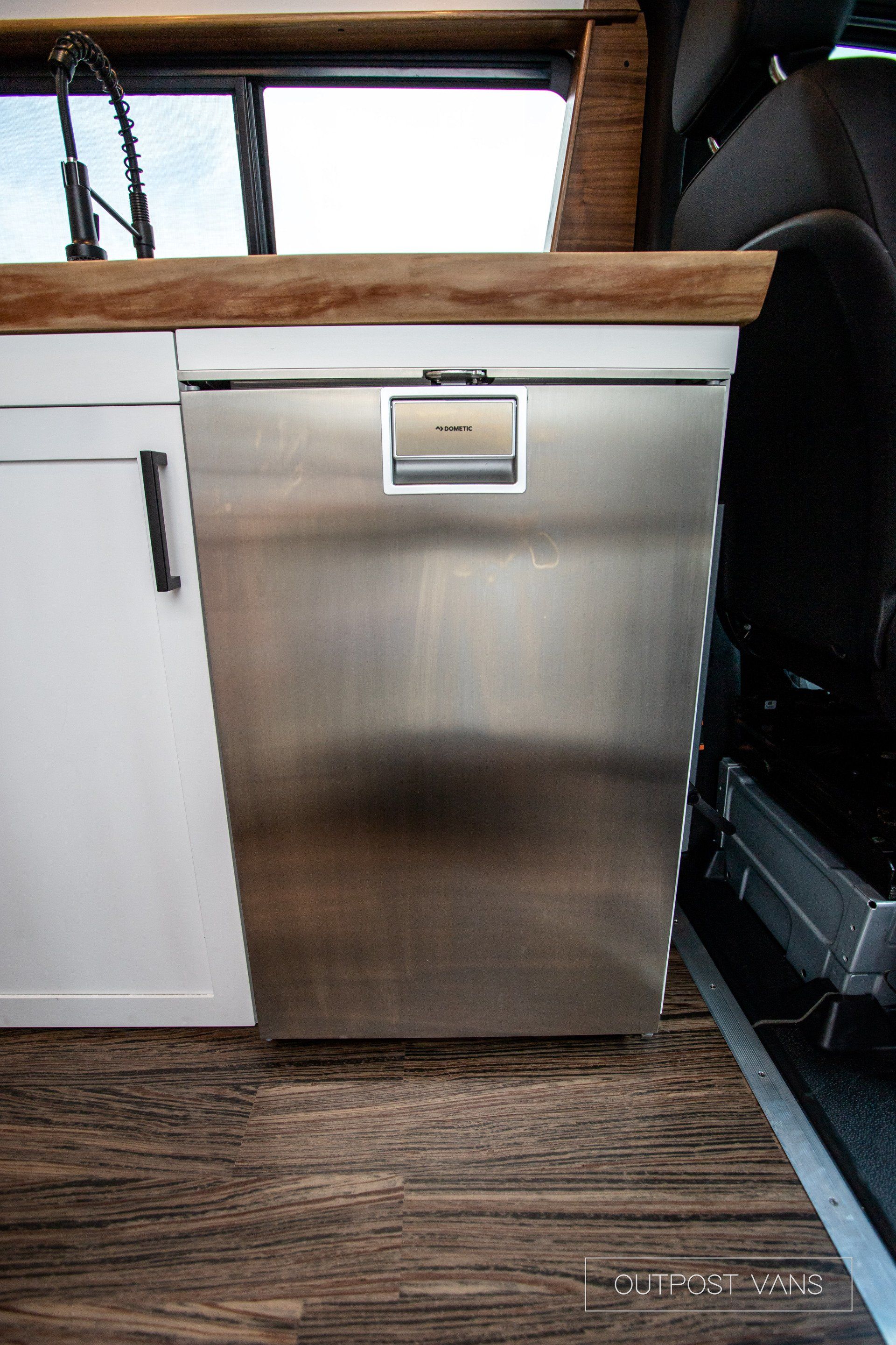 A stainless steel refrigerator is sitting under a wooden counter in a kitchen.